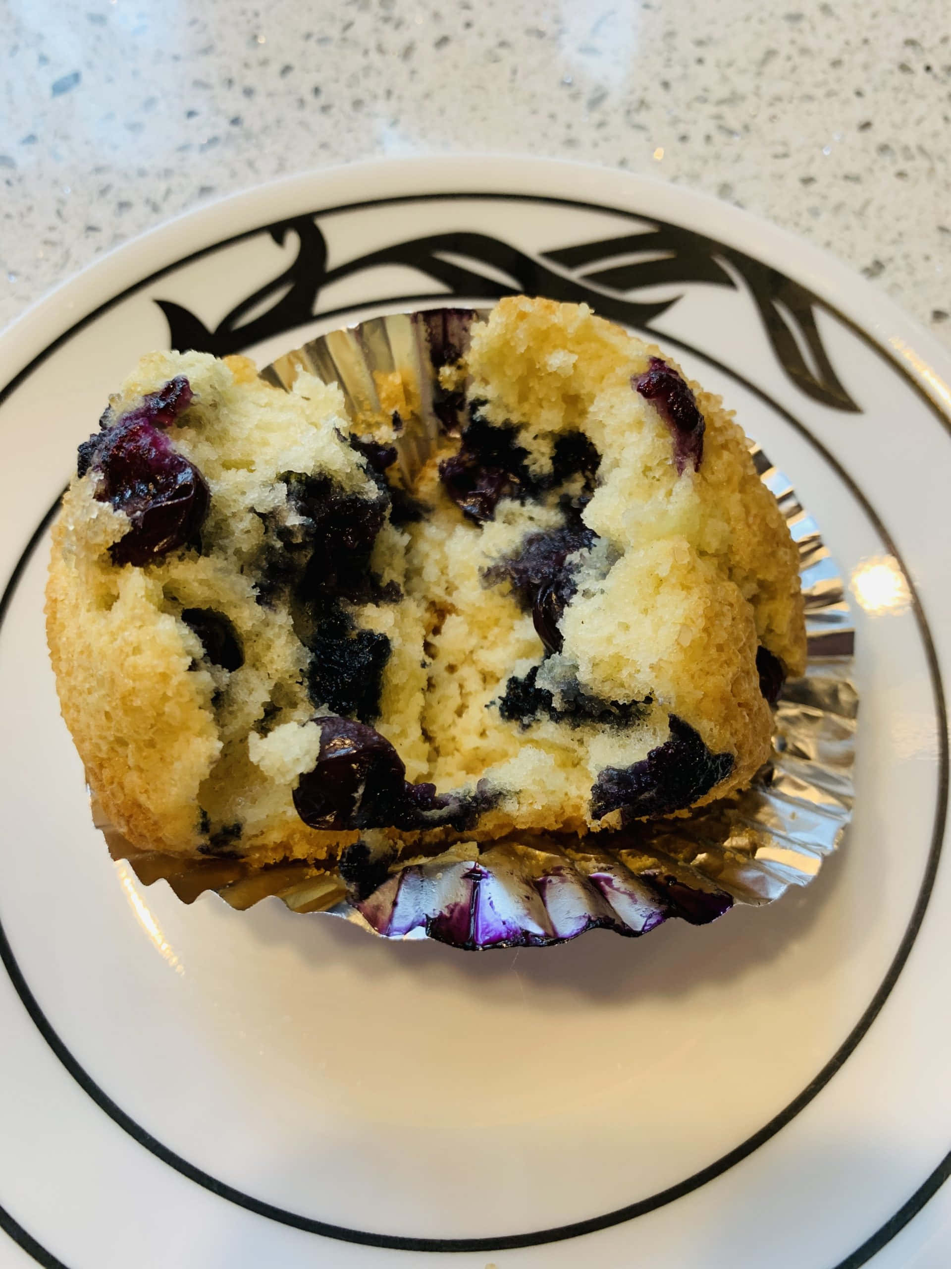 Blueberry Muffins 桌布 壁紙 — 一個金黃色的藍莓鬆餅被撕開，露出多汁的莓果和柔軟的碎屑，放在有圖案的碟子上。