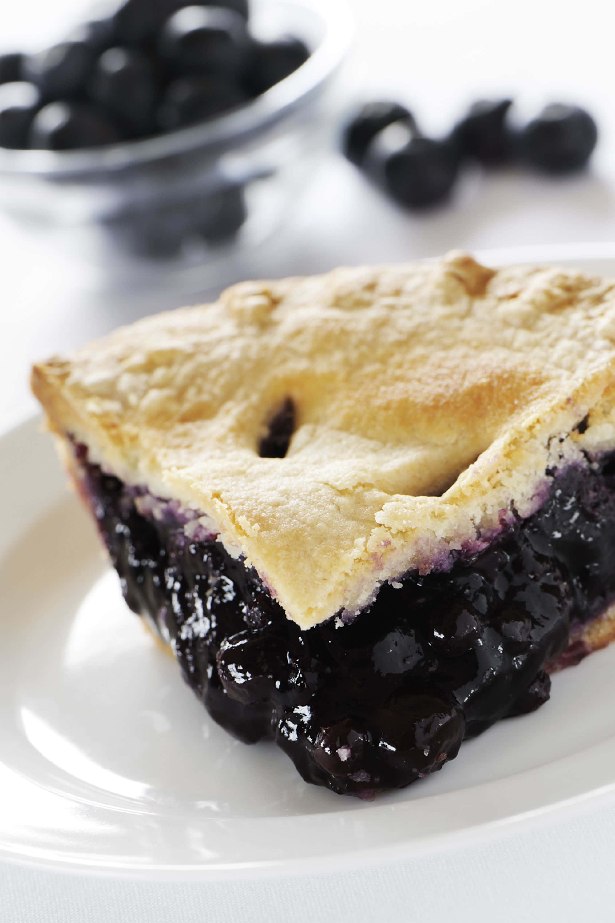 Blueberry Pie 桌布 壁紙 — 一個金黃色藍莓批切件的特寫，帶有豐富的餡料，放在白色碟子上。