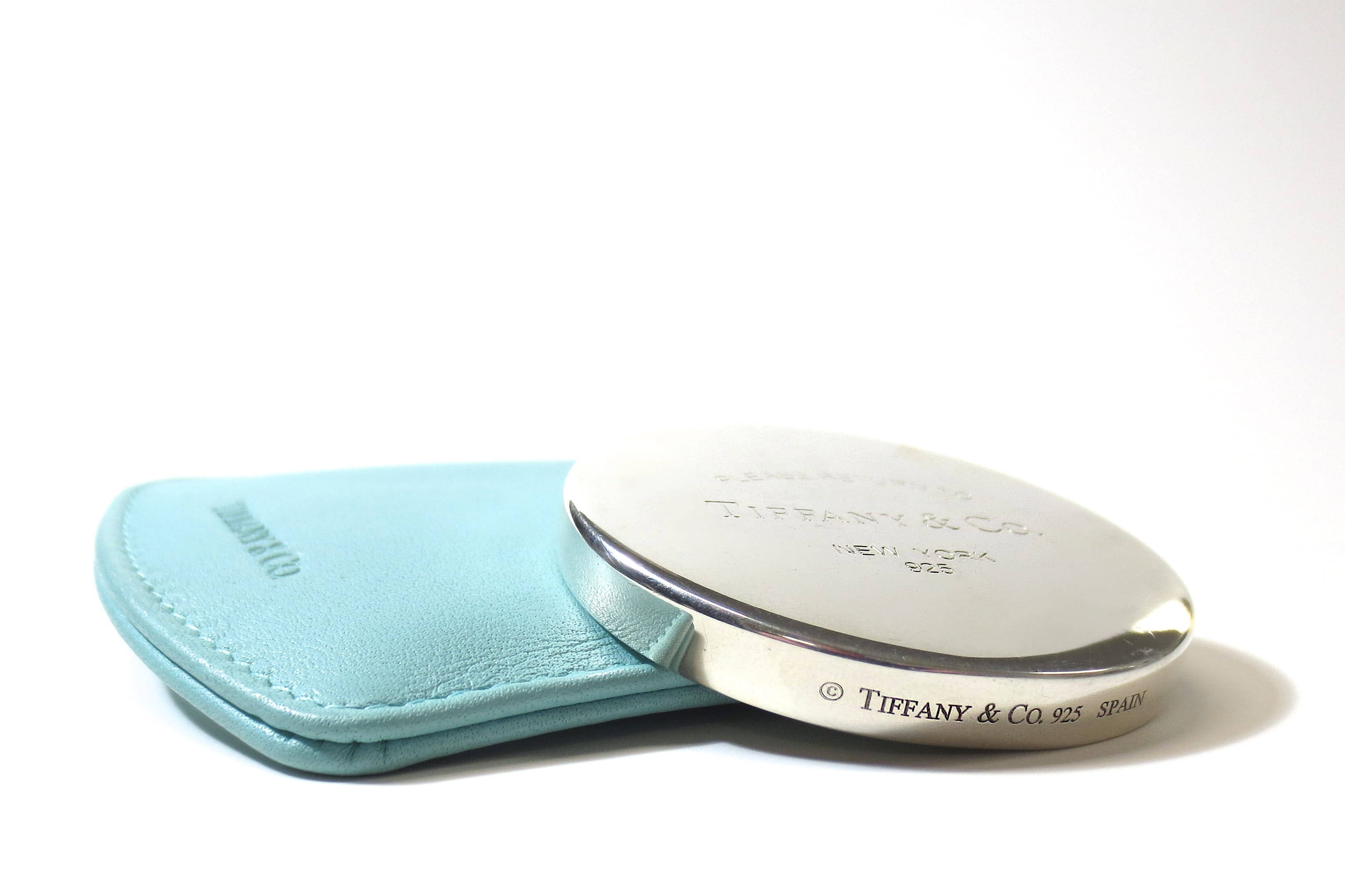 Authentic 桌布 壁紙 — 一個銀色Tiffany & Co.粉盒放在其淺藍色皮套旁邊，背景為純白色。