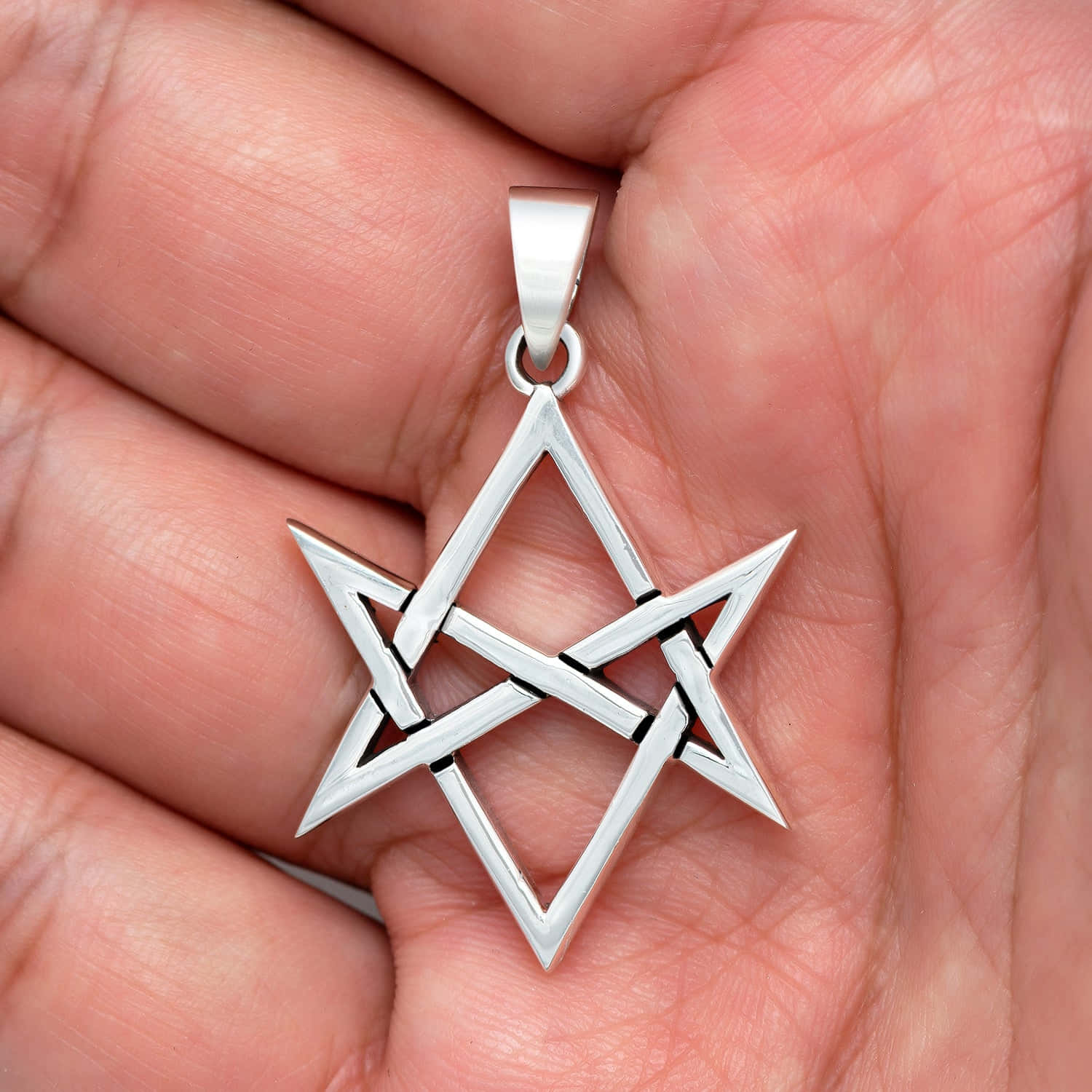 Thelema 桌布 壁紙 — 一個銀色五角星吊墜，帶有交錯的三角形，靜置於手掌中，捕捉柔和光線。