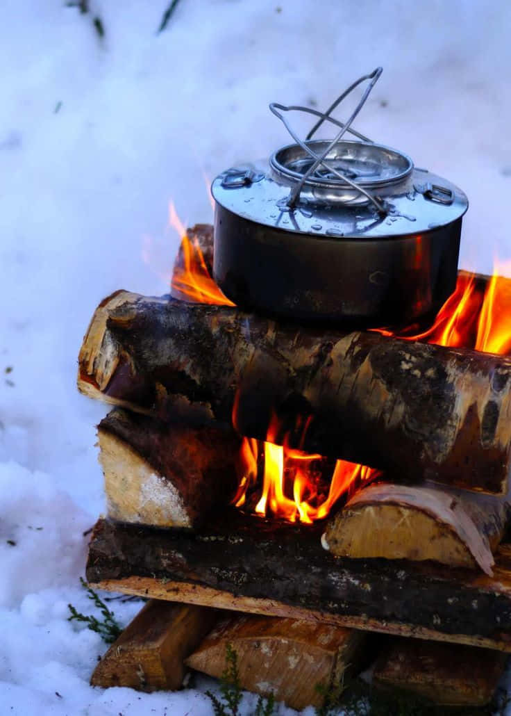 Winter Camping 桌布 壁紙 — 一個鍋放在雪地冬季景觀中用圓木搭建的熊熊營火上。