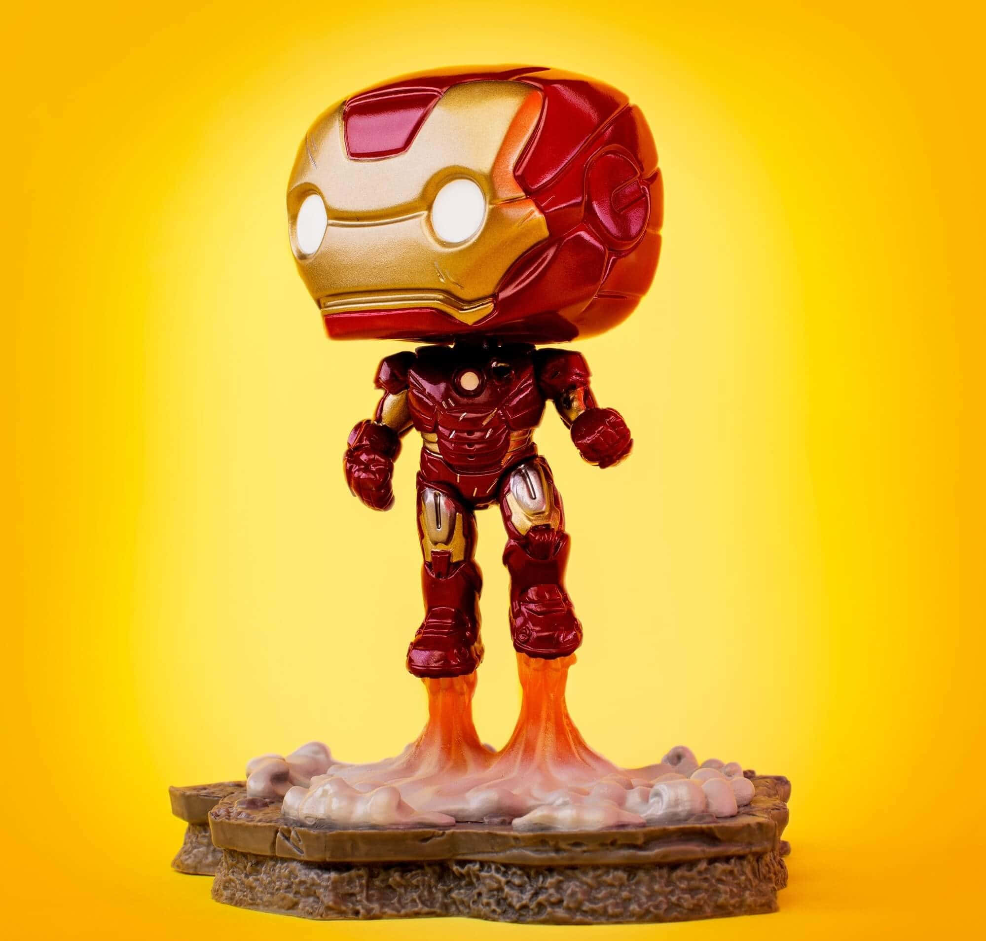Iron Man Pop Figures 桌布 壁紙 — 一個鐵甲奇俠的Funko Pop!人偶站在岩石底座上，雙腳發光，背景是鮮豔的黃色漸變。