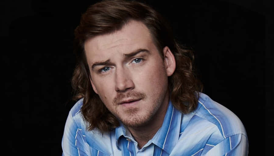 Morgan Wallen 桌布 壁紙 — 一個長著棕色長髮和藍色眼睛的男人，穿著藍色條紋襯衫，在黑色背景前專注地凝視著鏡頭。