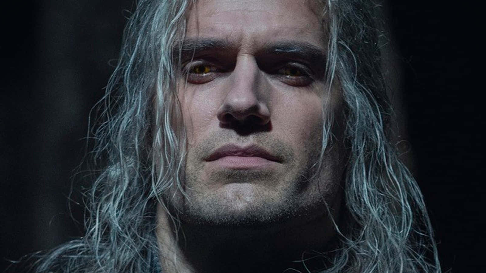 The Witcher Characters 桌布 壁紙 — 一個長著銀色長髮和發光琥珀色眼睛的男人特寫，在黑暗背景下強烈凝視。