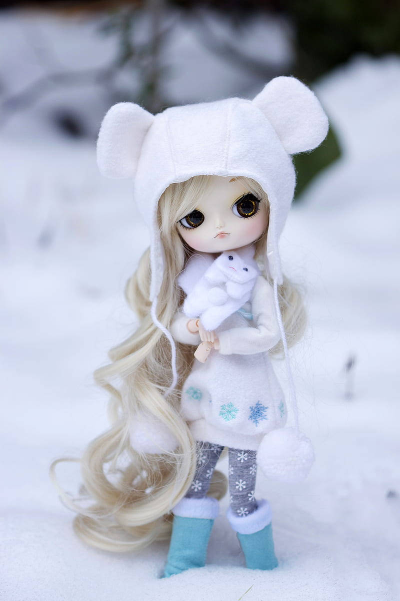 Doll 桌布 壁紙 — 一個長金髮的娃娃穿著白色熊帽套裝，站在深雪中，抱著一個毛絨雪兔。