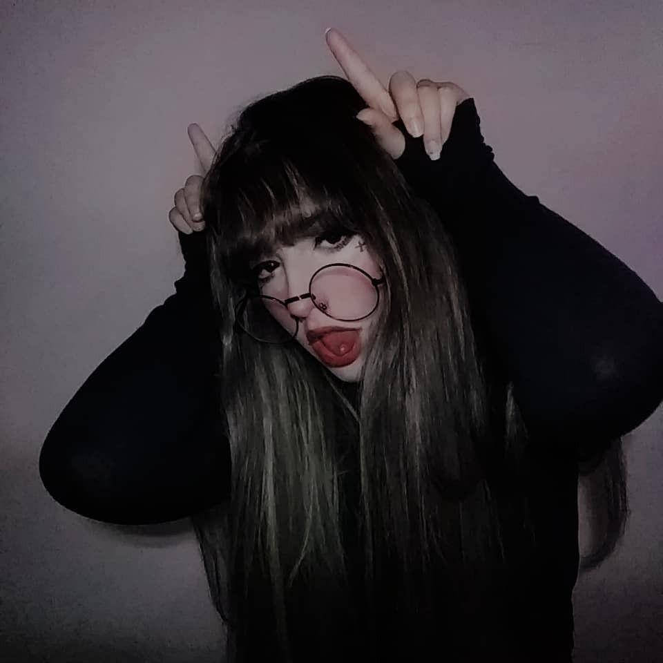 Grunge Aesthetic 桌布 壁紙 — 一個長黑髮戴眼鏡的人，對着素牆做出鬼臉，同時舉起魔鬼角。