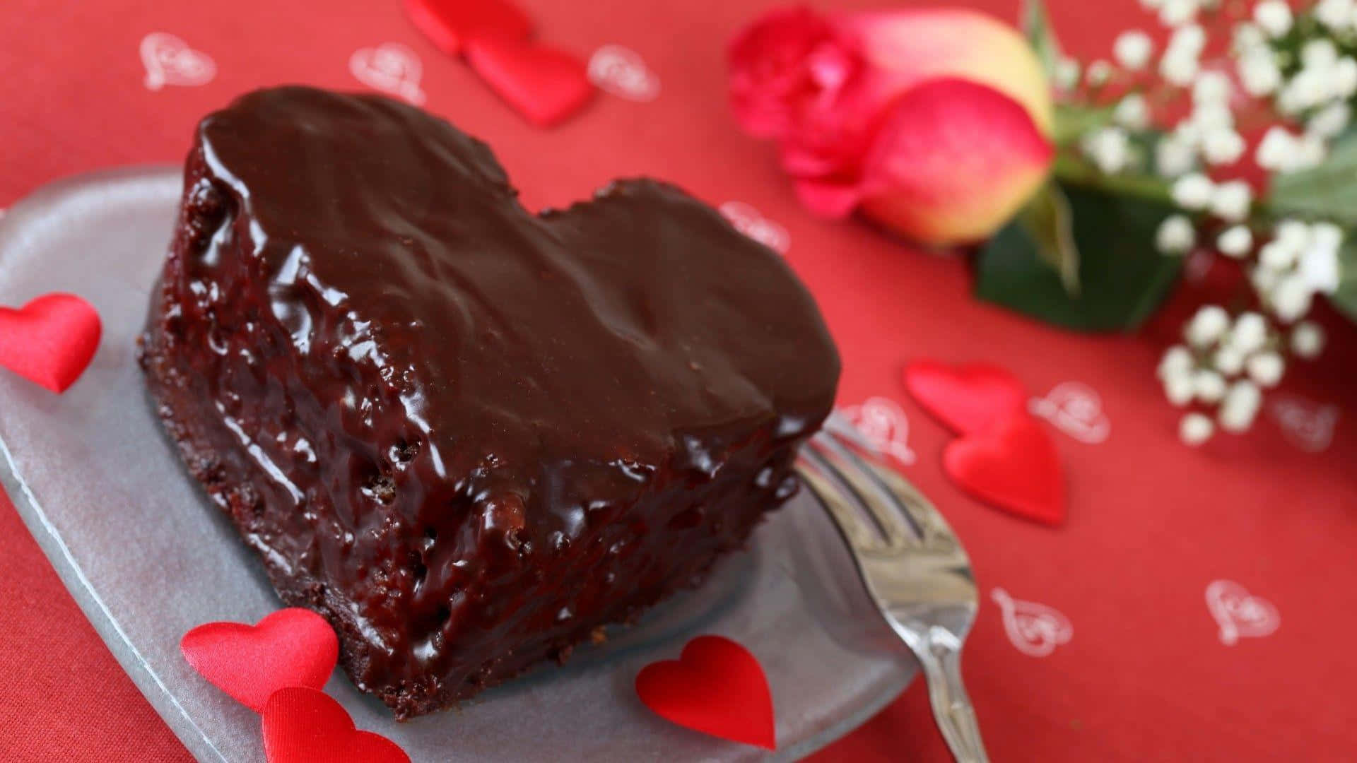 Chocolate Cake 桌布 壁紙 — 一個閃亮的朱古力心形蛋糕放在銀碟上，周圍有紅心和玫瑰，放在紅色枱布上。