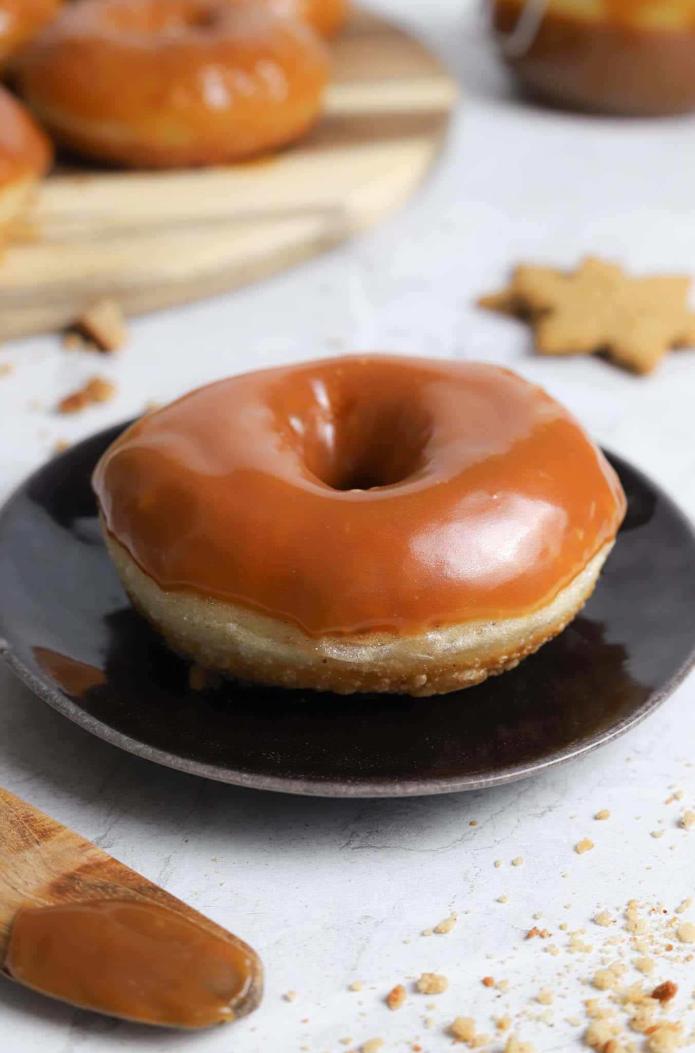 Glazed Donut 桌布 壁紙 — 一個閃亮的焦糖釉面冬甩放在深色碟上，旁邊有散落的碎屑和星形曲奇。