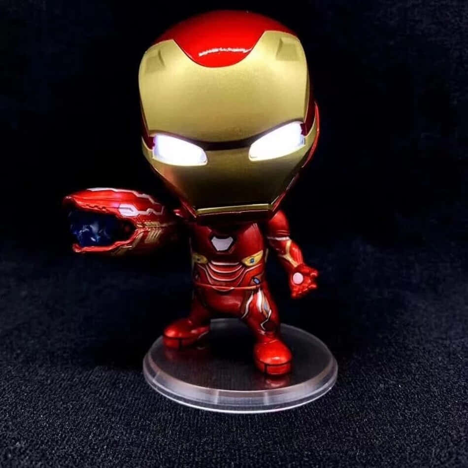 Iron Man Bobbleheads 桌布 壁紙 — 一個閃亮的紅色和金色鐵甲奇俠人偶站在透明底座上，手持無限手套，背景為深色紋理。