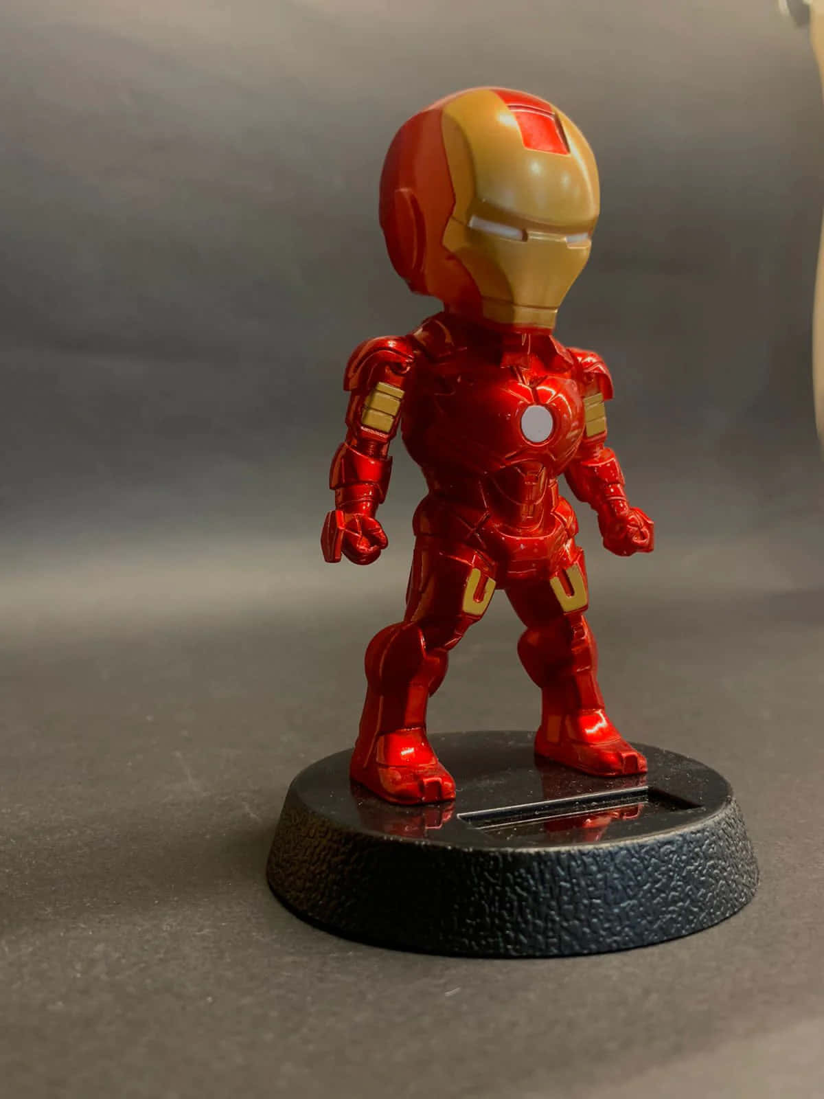 Iron Man Bobbleheads 桌布 壁紙 — 一個閃亮的紅色和金色鐵甲奇俠人偶站在黑色紋理底座上，背景為柔和的灰色。