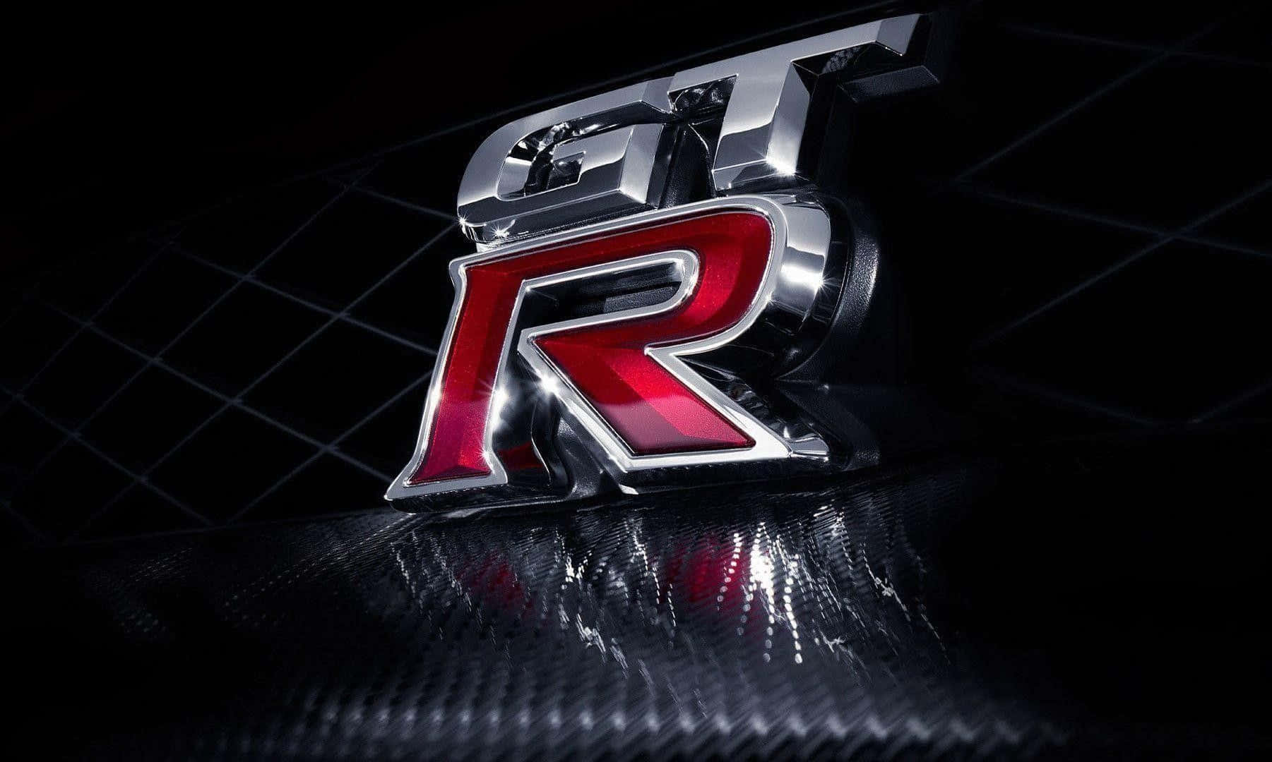 Car Logo 桌布 壁紙 — 一個閃亮的鍍鉻和紅色GT-R徽章在戲劇性的工作室燈光下，放置在帶有紋理的碳纖維表面上。
