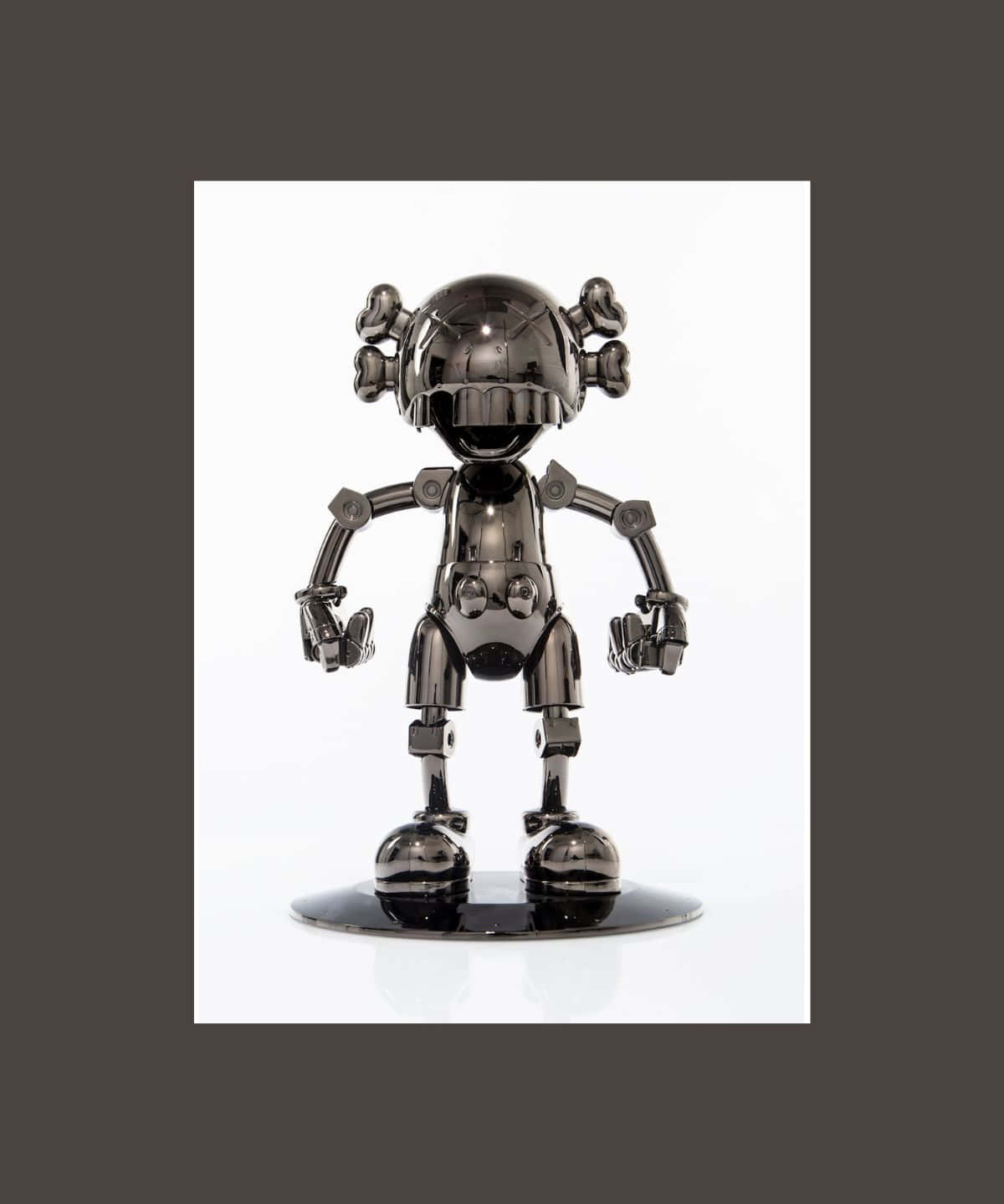 Kaws Figures 桌布 壁紙 — 一個閃亮的黑色鉻合金機械人公仔，頭部像骷髏，四肢有關節，站在一個反射底座上，背景是純白色。