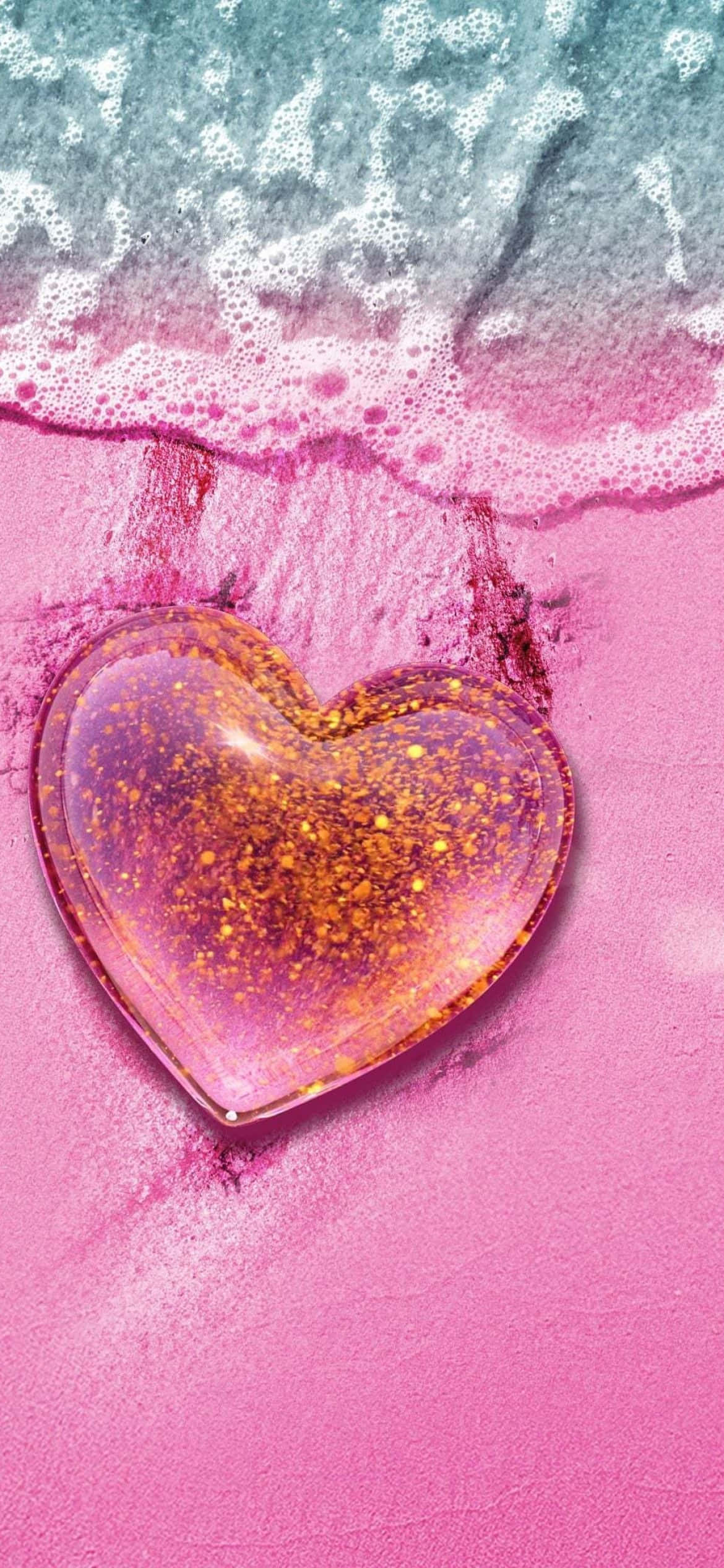 Beach Love 桌布 壁紙 — 一個閃閃發光的心形玻璃物件放在粉紅色的沙子上，綠松石色的海浪帶著白色泡沫輕輕拍打著它。