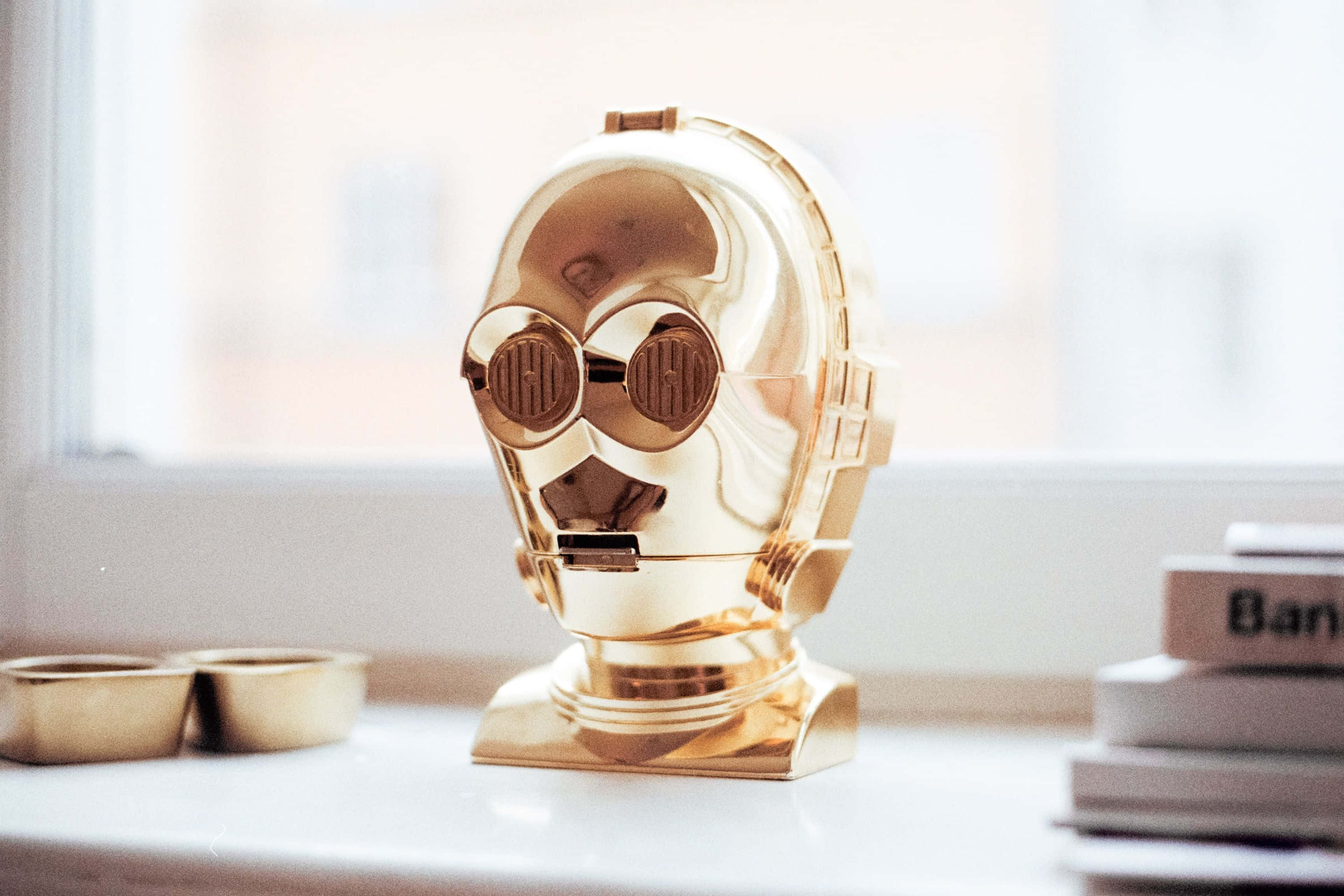 C-3po 桌布 壁紙 — 一個閃閃發光的金色C-3PO頭像模型放在窗台上，旁邊有書本和小金碗。