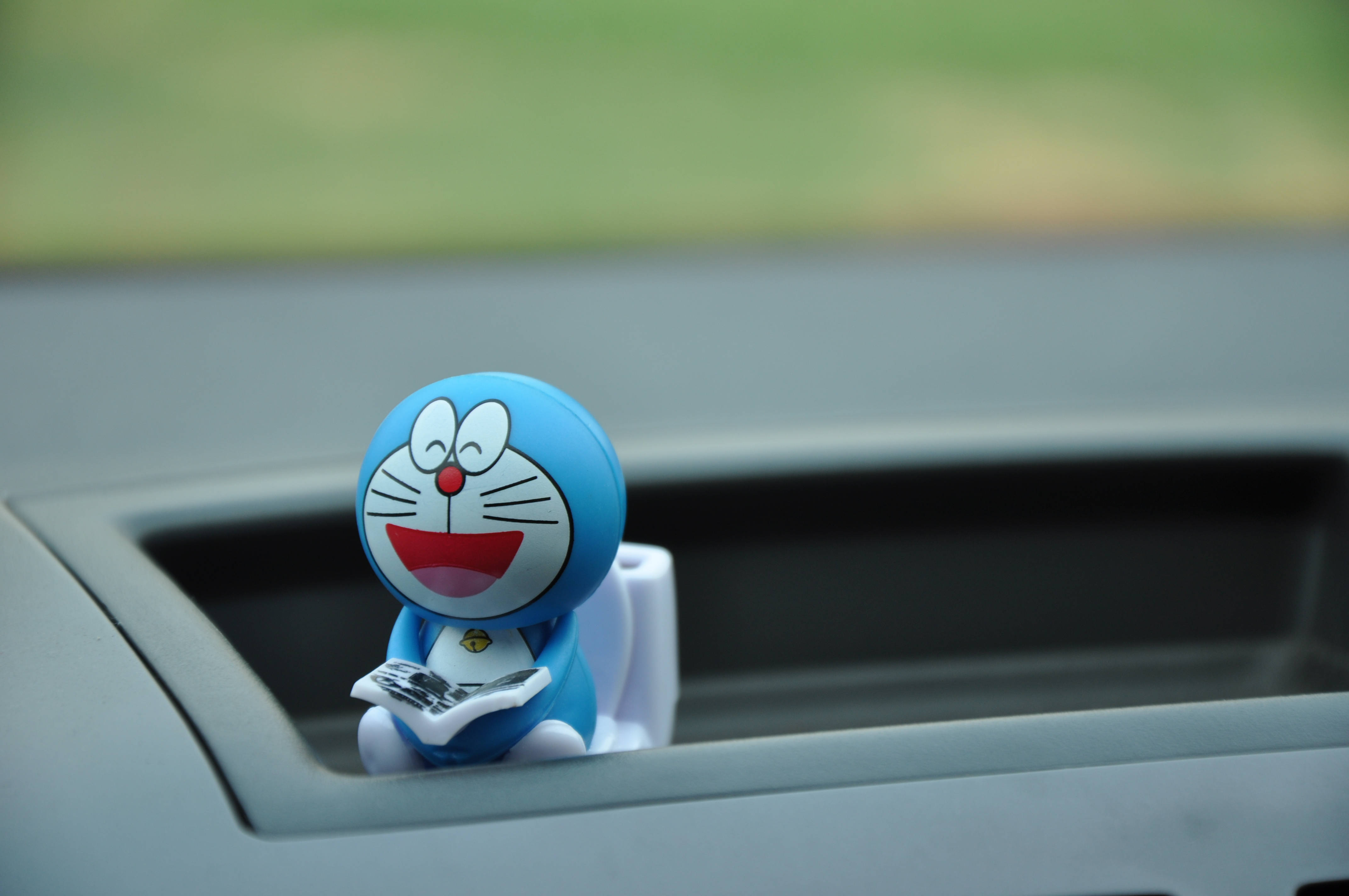 Doraemon 桌布 壁紙 — 一個開心的藍色多啦A夢公仔坐在汽車杯架上閱讀報紙，背景是模糊的綠色。
