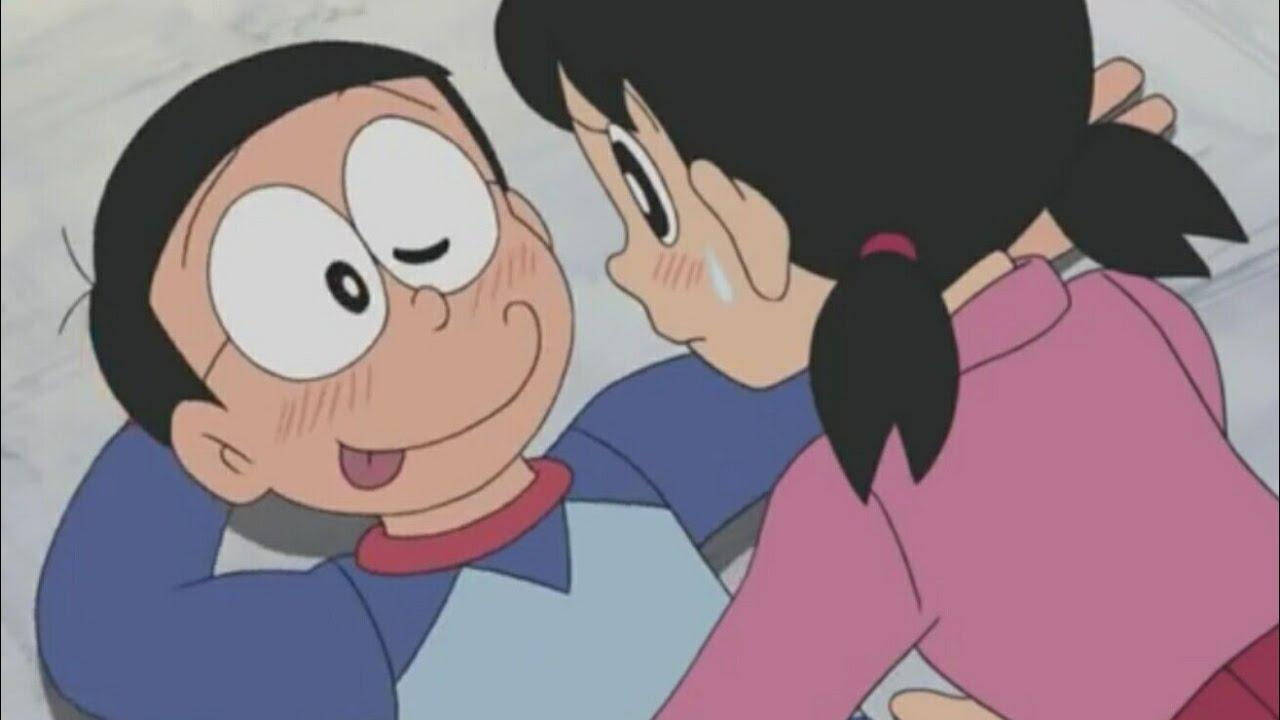 nobita shizuka love 桌布 壁紙 — 一個開朗的動畫男孩，大眼睛微笑著，而一個穿粉紅色衣服的女孩靠得很近，兩人都分享著溫暖、親密的時刻。