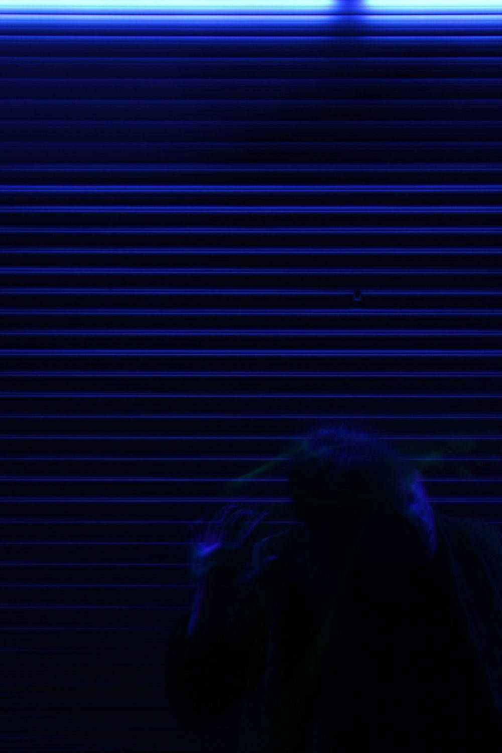 lines 桌布 壁紙 — 一個陰暗的身影站在發光的藍色捲簾前，沐浴在霓虹燈光中。