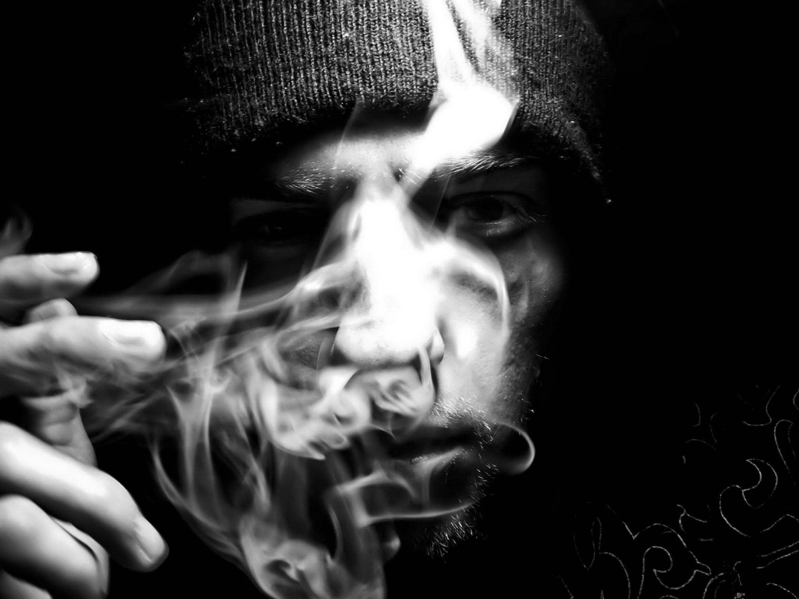 黑白 桌布 壁紙 — 一個陰鬱的黑白肖像，一個戴著無邊帽的男人在黑暗背景下呼出煙霧，煙霧在他的臉上旋轉。