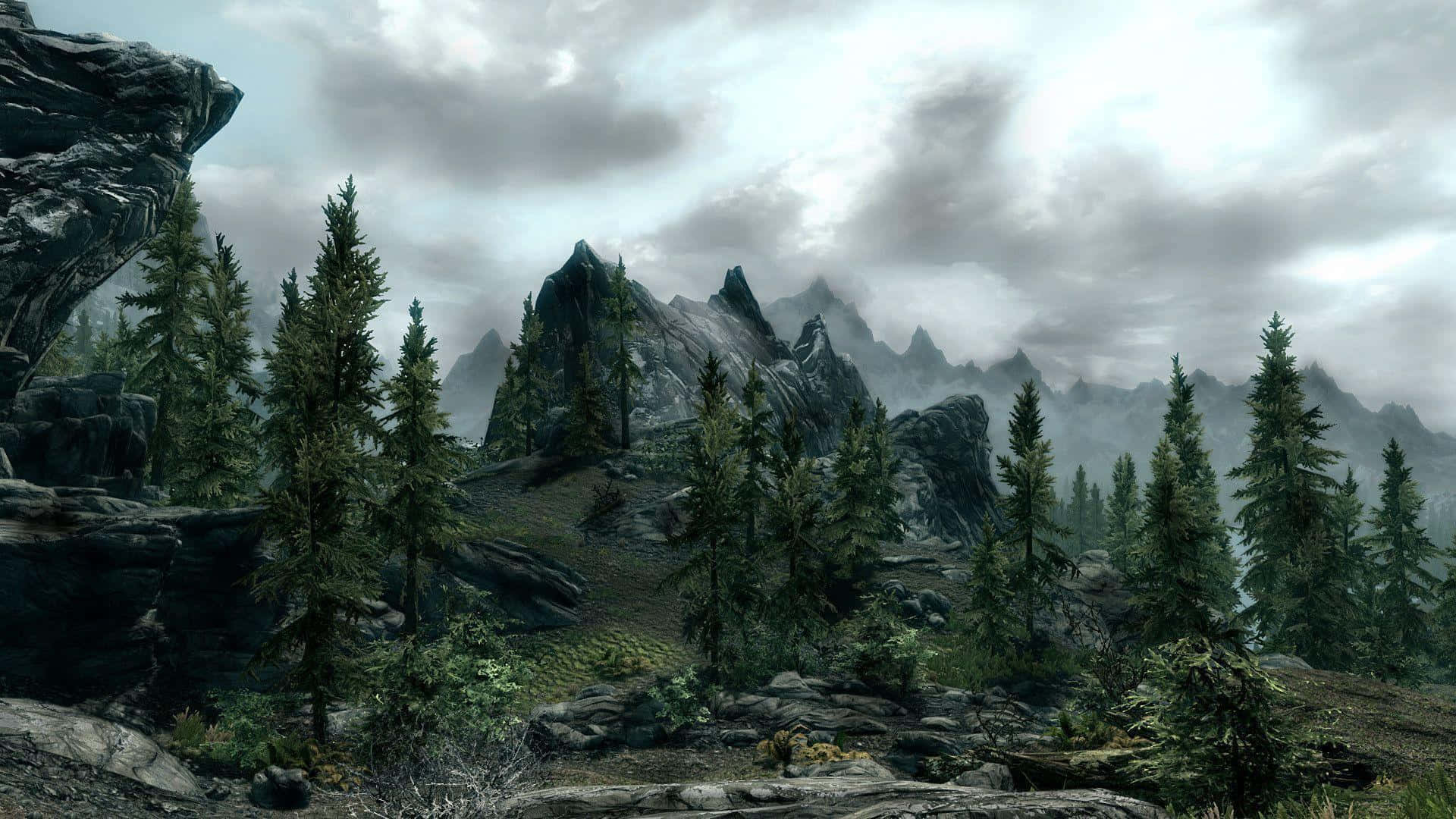 Skyrim Landscapes 桌布 壁紙 — 一個霧氣瀰漫的山景，有鋸齒狀的山峰和常青樹，天空多雲。