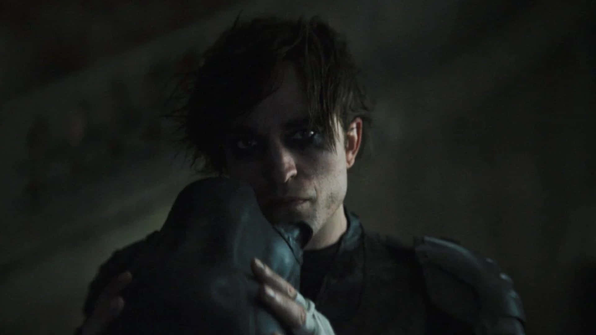 Bruce Wayne 桌布 壁紙 — 一個面容陰沉、身穿暗色鎧甲的男人在陰暗、充滿氛圍的環境中緊握著頭盔。
