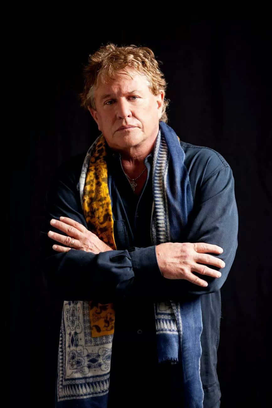 Tom Berenger 桌布 壁紙 — 一個頭髮凌亂的男人站在黑色背景前，雙手交叉，戴著圖案圍巾和深色襯衫。
