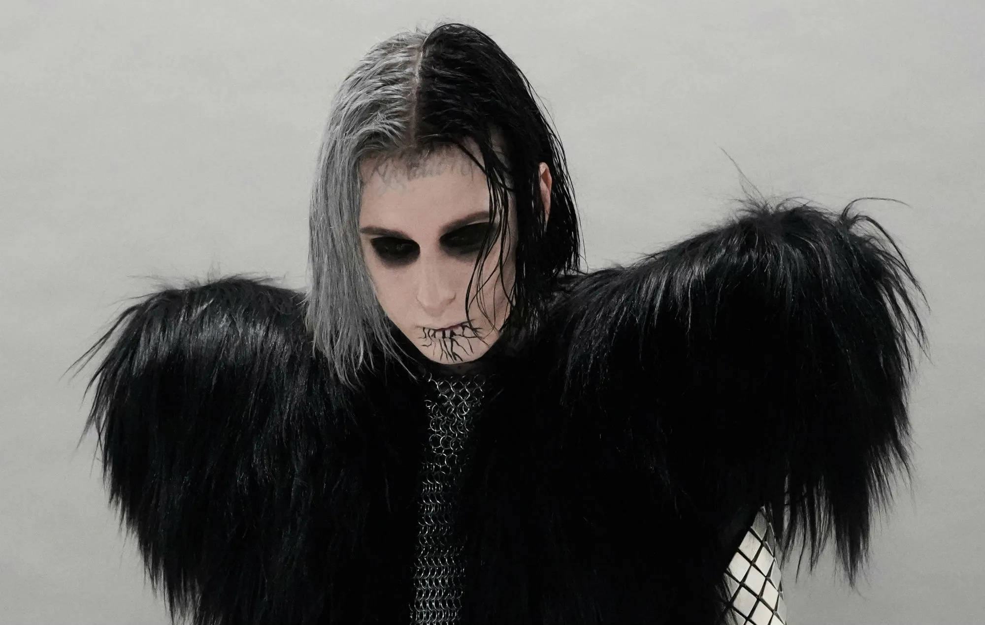 Ghostemane 桌布 壁紙 — 一個頭髮半黑半銀、化著深色妝容的人，在純灰色背景前穿著黑色毛絨外套。