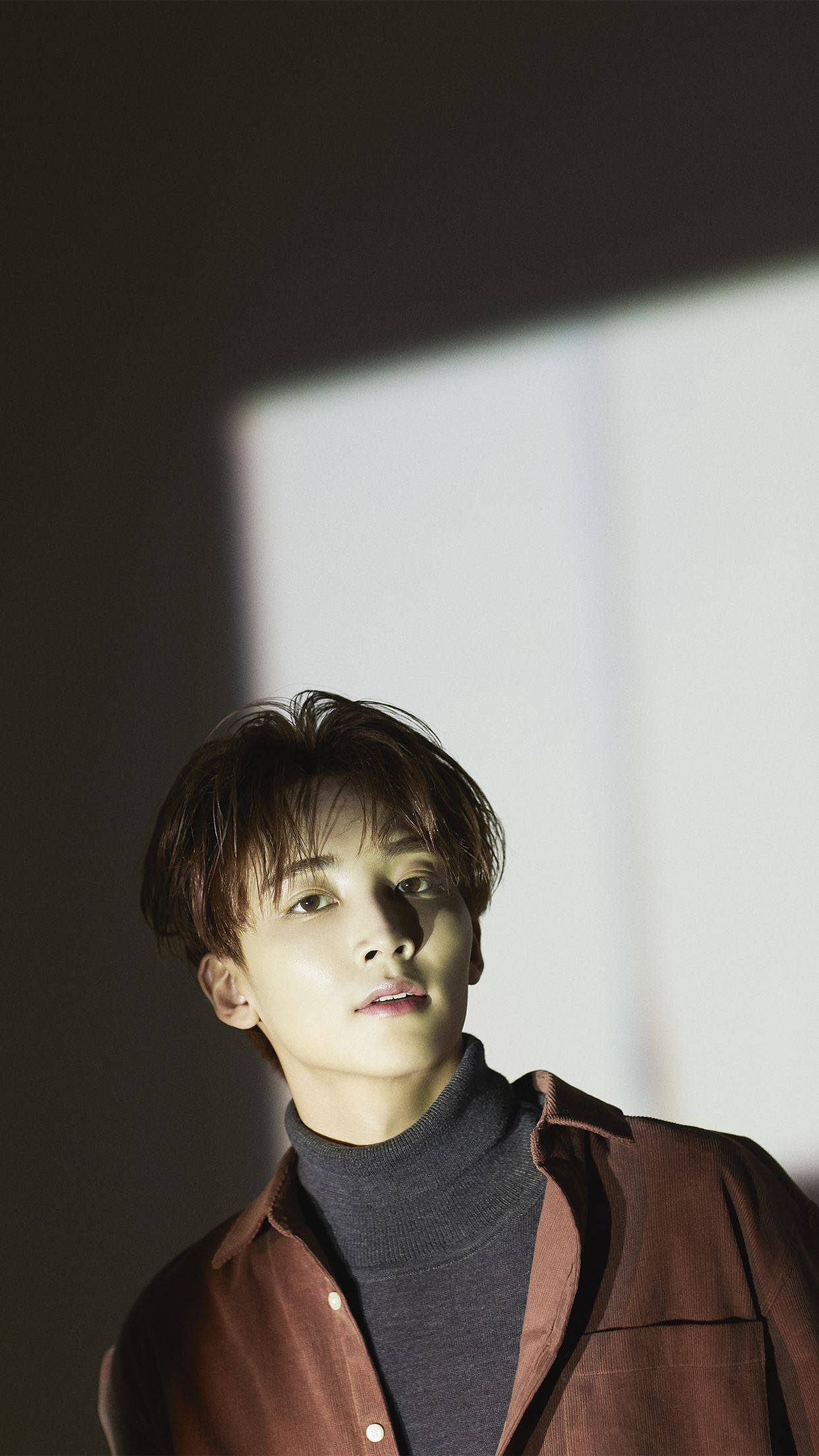Yoon Jeonghan Director's Cut 壁紙 — 一個頭髮蓬鬆的年輕男子在柔和的工作室燈光下向上凝視，一道明亮的矩形光束投射在他的臉和棕色襯衫上。