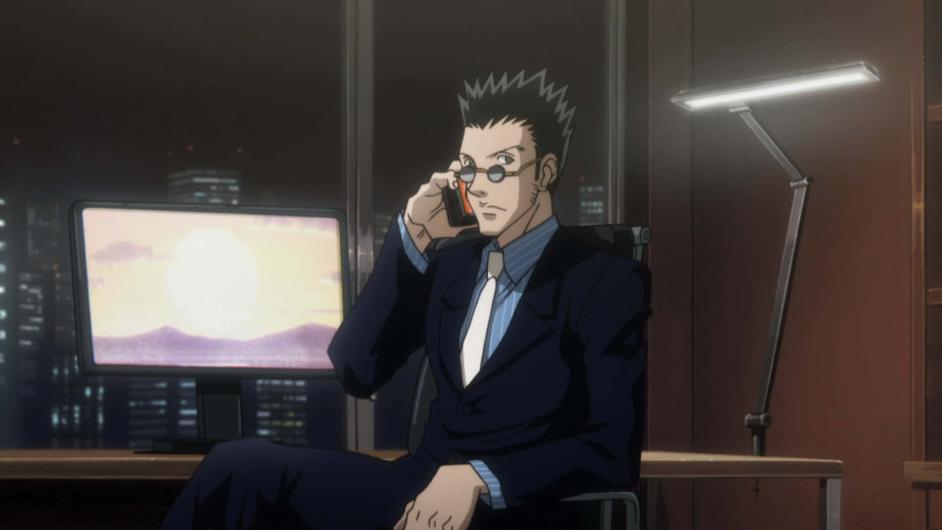 Leorio Paradinight 桌布 壁紙 — 一個頭髮豎起的動漫男人穿著西裝在昏暗的辦公室裡講電話，顯示器上顯示著城市日落景色。