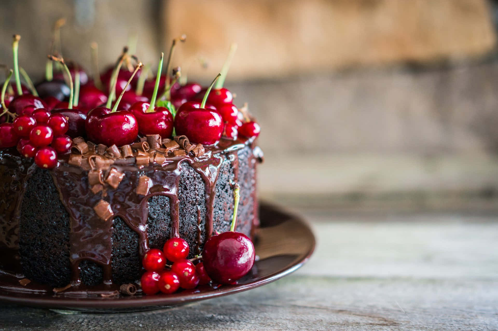 Black Forest Cake 桌布 壁紙 — 一個頹廢的巧克力蛋糕滴著光亮的甘納許，並在質樸的木桌上飾以鮮豔的紅櫻桃和蔓越莓。