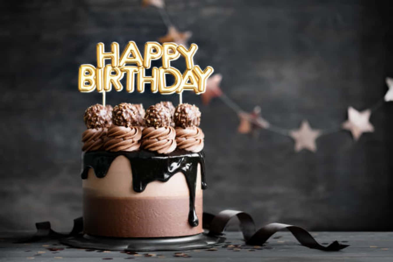 生日蛋糕 桌布 壁紙 — 一個頹廢的朱古力生日蛋糕，帶有金色字母裝飾和星星花環，背景為深色紋理。
