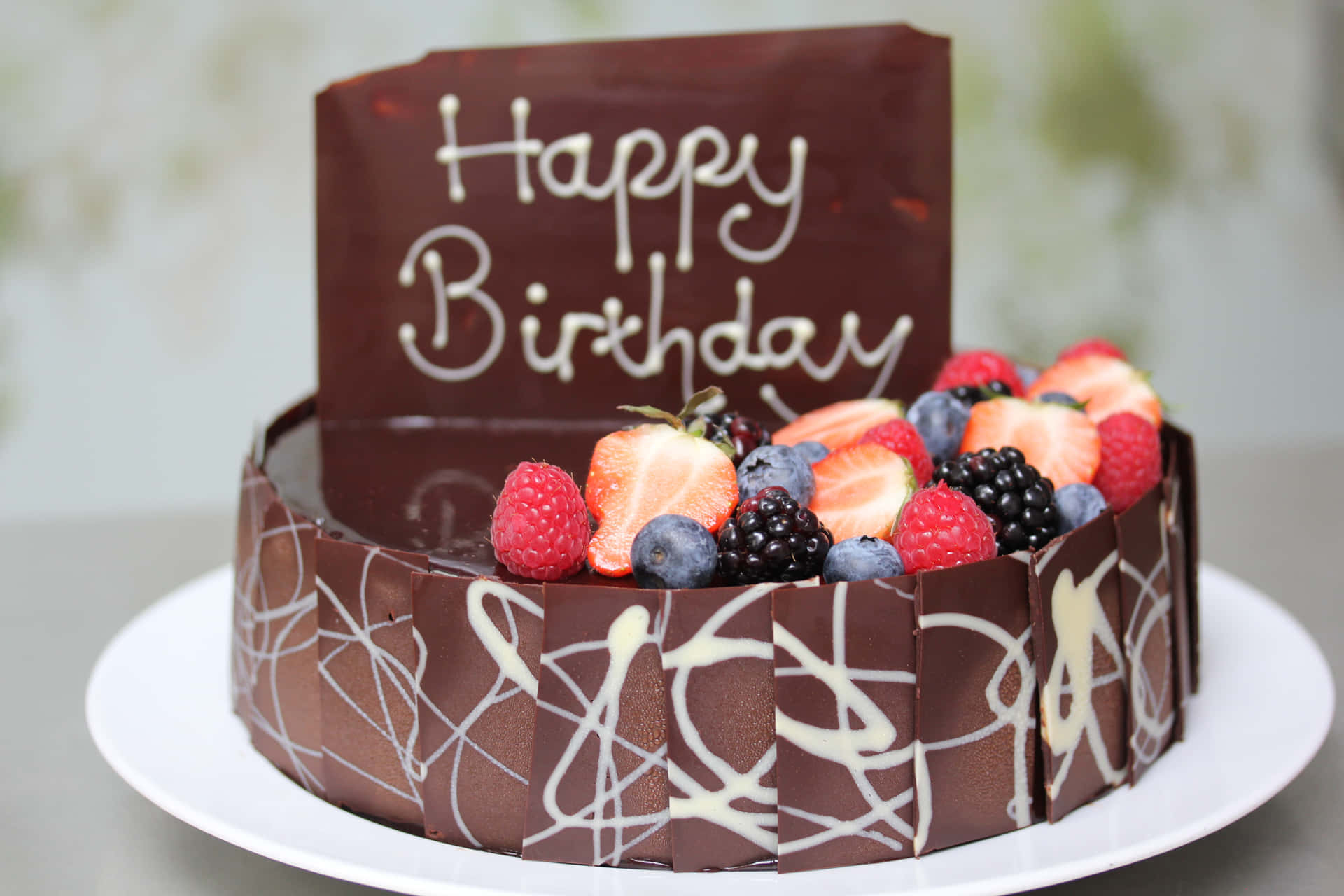  壁紙 — 一個頹廢的朱古力生日蛋糕，飾以新鮮漿果和一個寫著 'Happy Birthday' 的光澤朱古力牌。