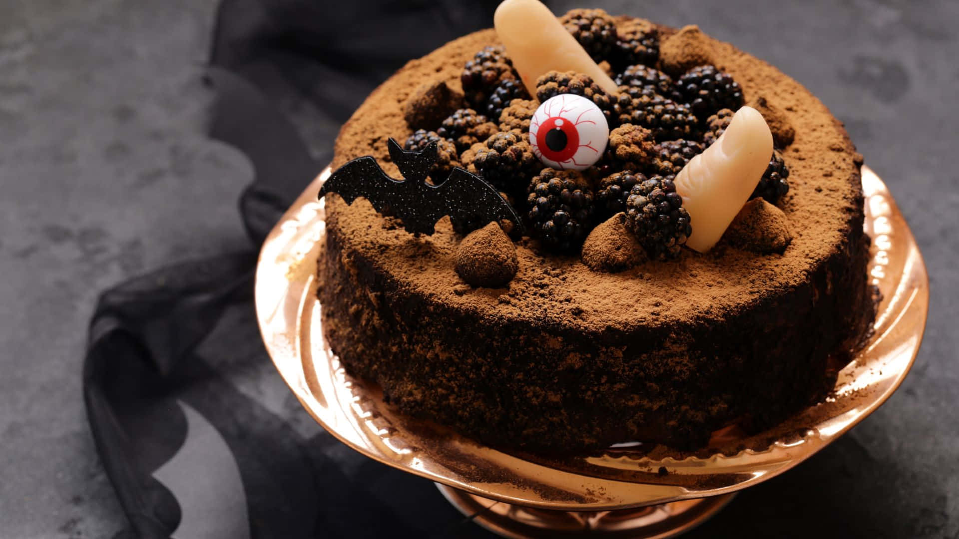 Halloween Cake 桌布 壁紙 — 一個頹廢的朱古力蛋糕，撒上可可粉，上面放有黑莓、假手指和一個金架上的凸眼。