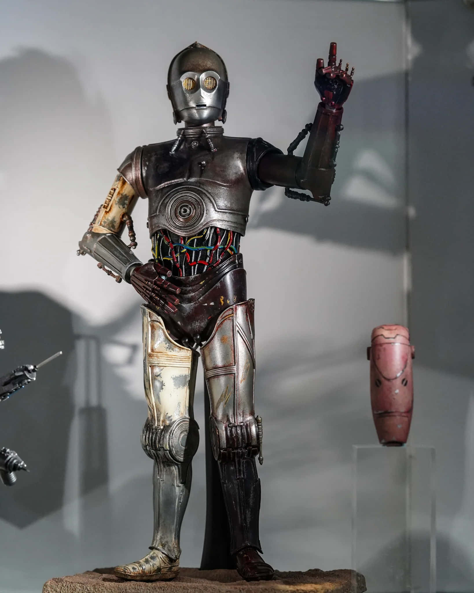 C-3po 桌布 壁紙 — 一個風化的C-3PO機械人雕像在博物館燈光下展出，帶有外露的電線和生鏽的金屬部件。