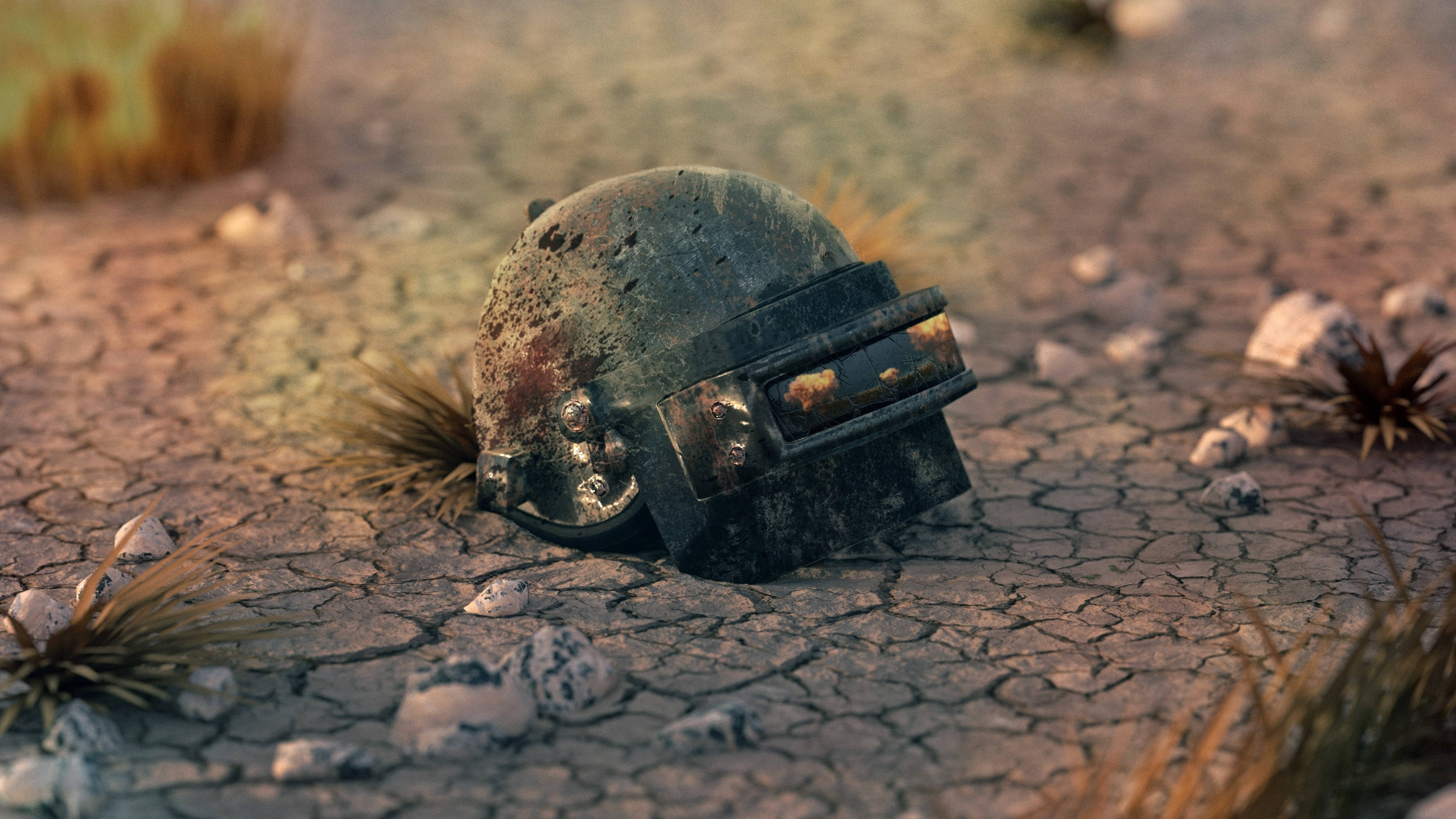 PUBG 桌布 壁紙 — 一個風化的戰鬥頭盔放在龜裂的沙漠土地上，周圍有稀疏的乾草和岩石，在溫暖的陽光下。