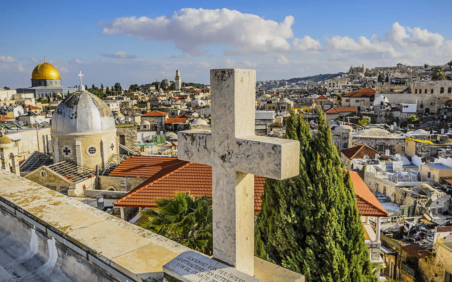 Holy Land 桌布 壁紙 — 一個風化的石十字架矗立在耶路撒冷的墓地，俯瞰著圓頂清真寺和古老的石建築，天空湛藍。