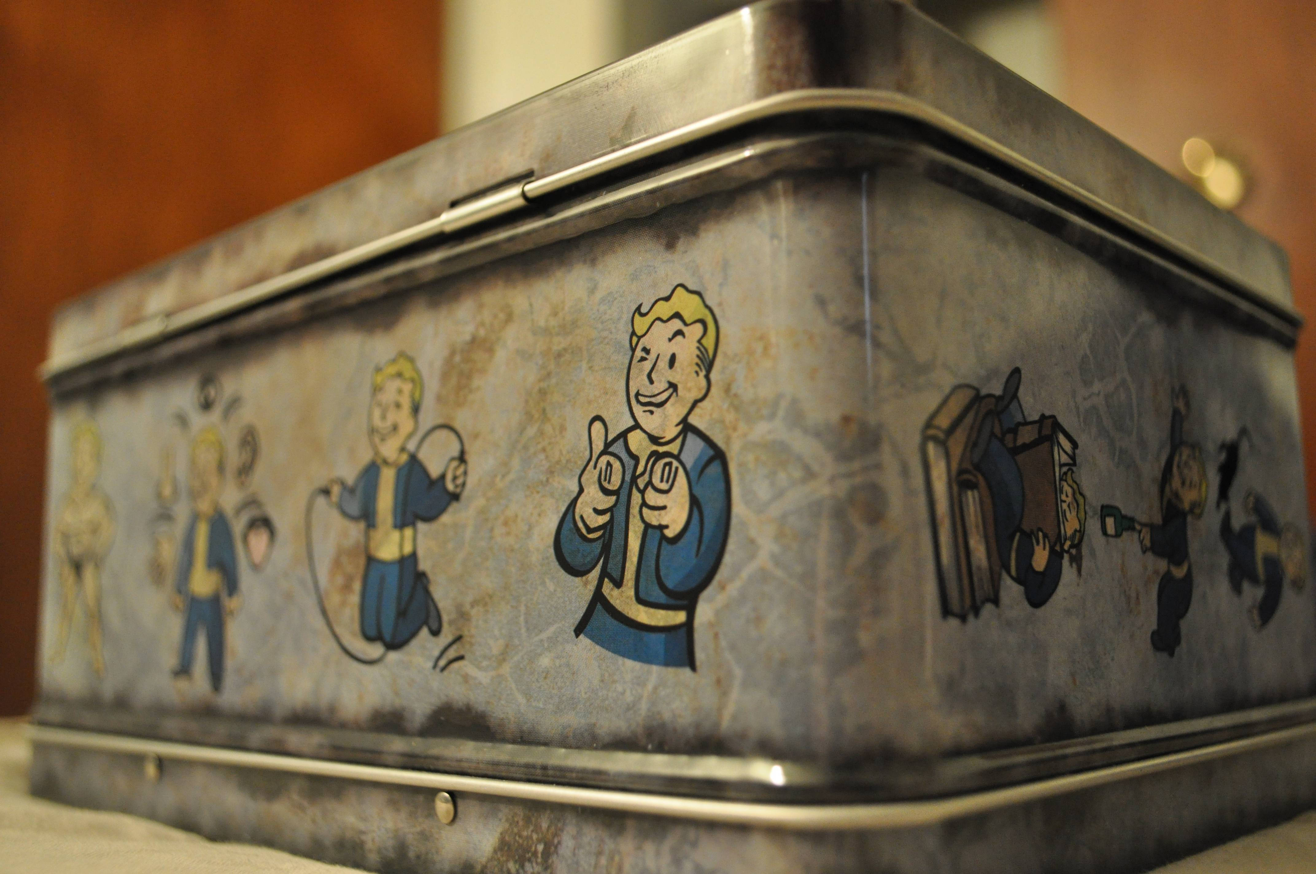 Fallout 4 桌布 壁紙 — 一個風化的金屬午餐盒，飾有經典的Fallout Vault Boy插圖，顯示出歲月和使用痕跡。