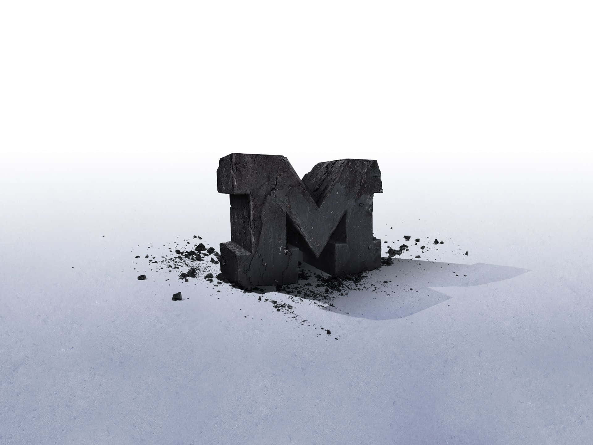 Michigan Wolverines 桌布 壁紙 — 一個風化的黑色石頭字母M從雪原中浮現，在明亮的日光下投下清晰的陰影。