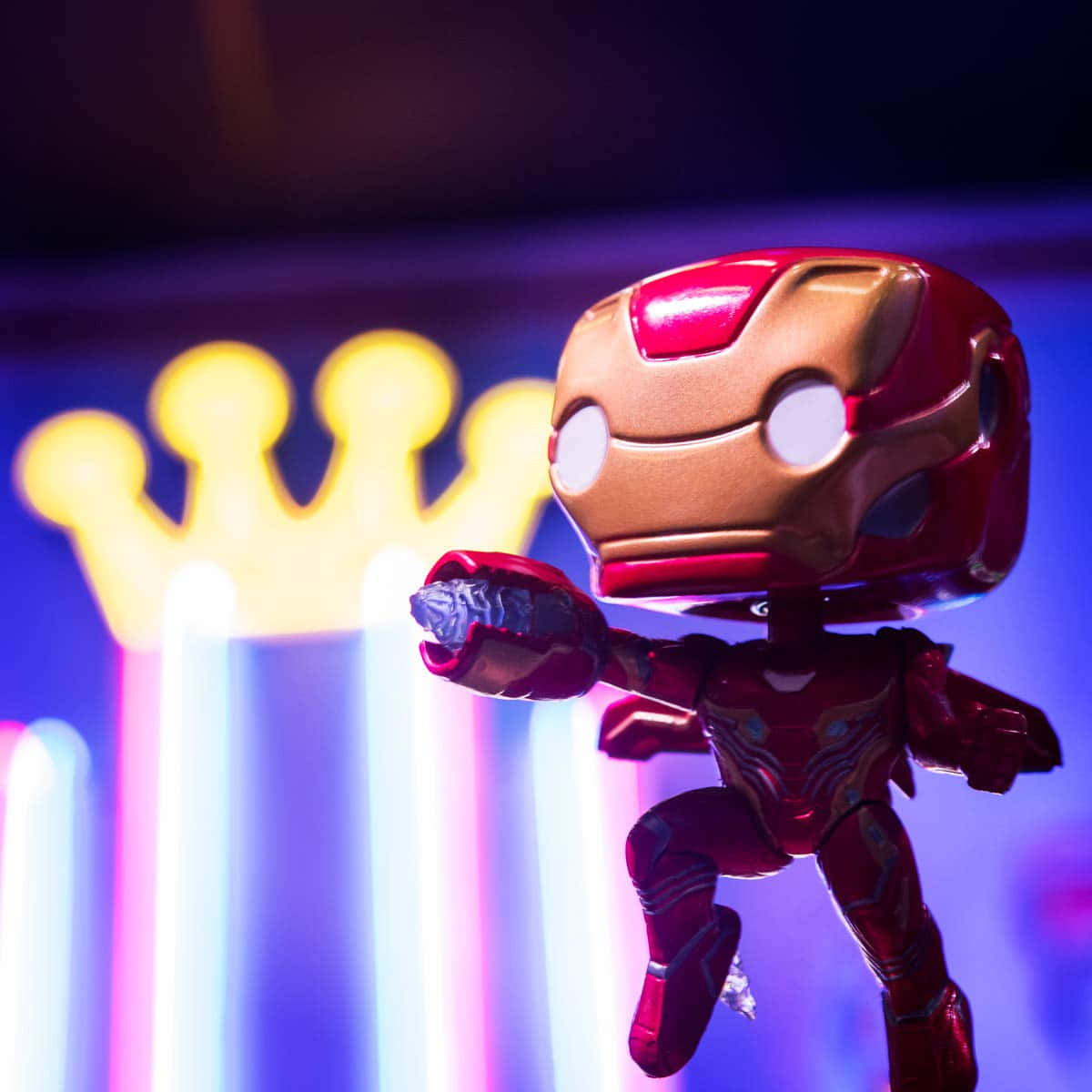 Iron Man Pop Figures 桌布 壁紙 — 一個風格化的鐵甲奇俠 Funko Pop 人偶在發光的霓虹皇冠背景前動態擺姿勢，帶有鮮豔的紫色和黃色燈光。
