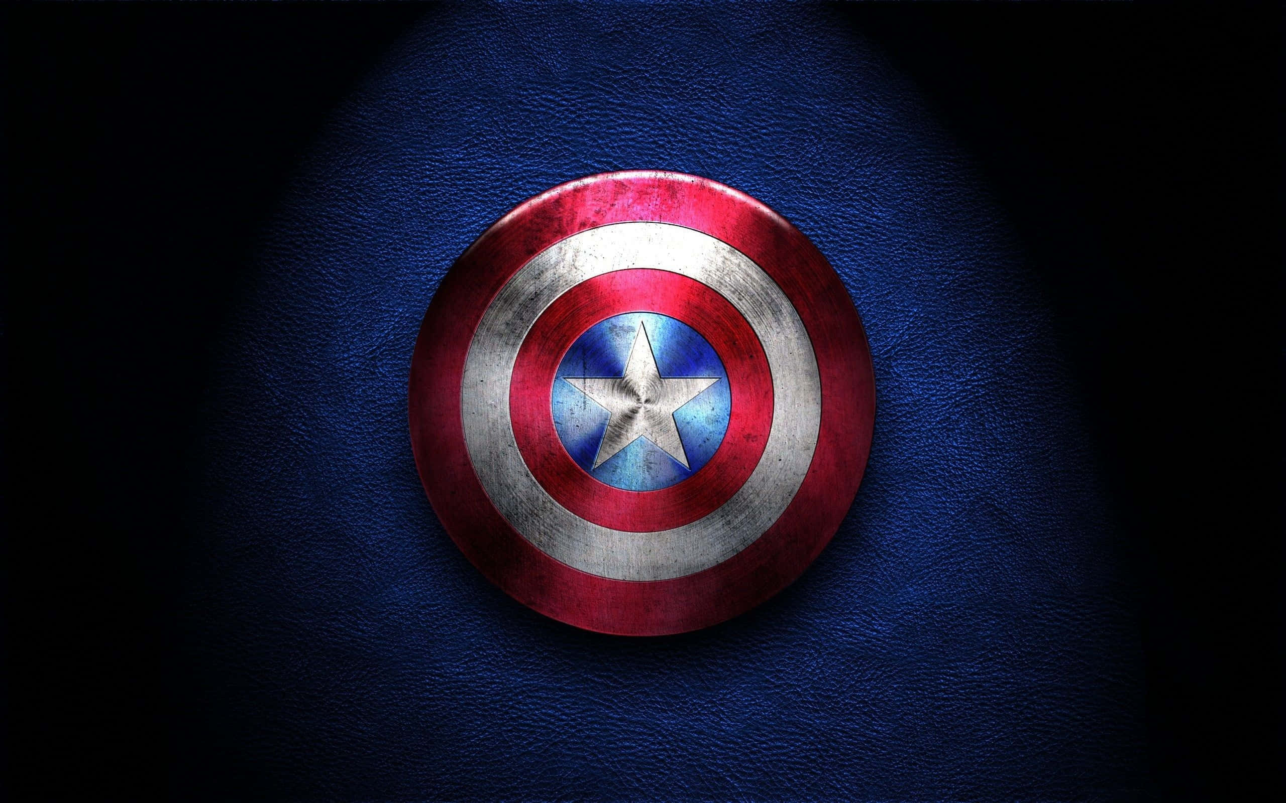 Best Captain America 桌布 壁紙 — 一個飽經風霜的美國隊長盾牌，在戲劇性的聚光燈下，放置在帶有紋理的藍色皮革上。