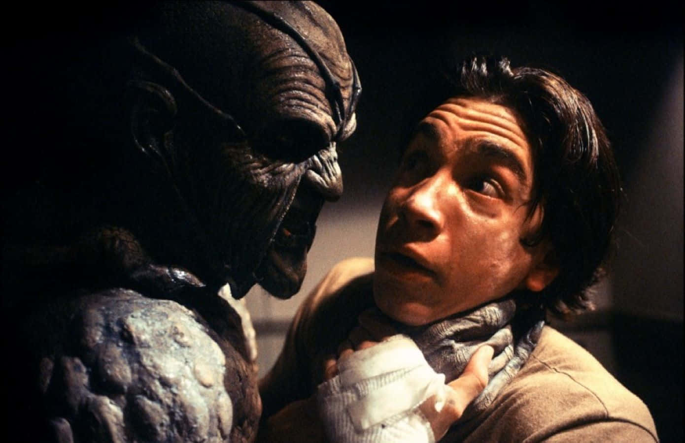 Justin Long 桌布 壁紙 — 一個驚恐的男人在昏暗的場景中被一個怪誕的外星生物勒頸。