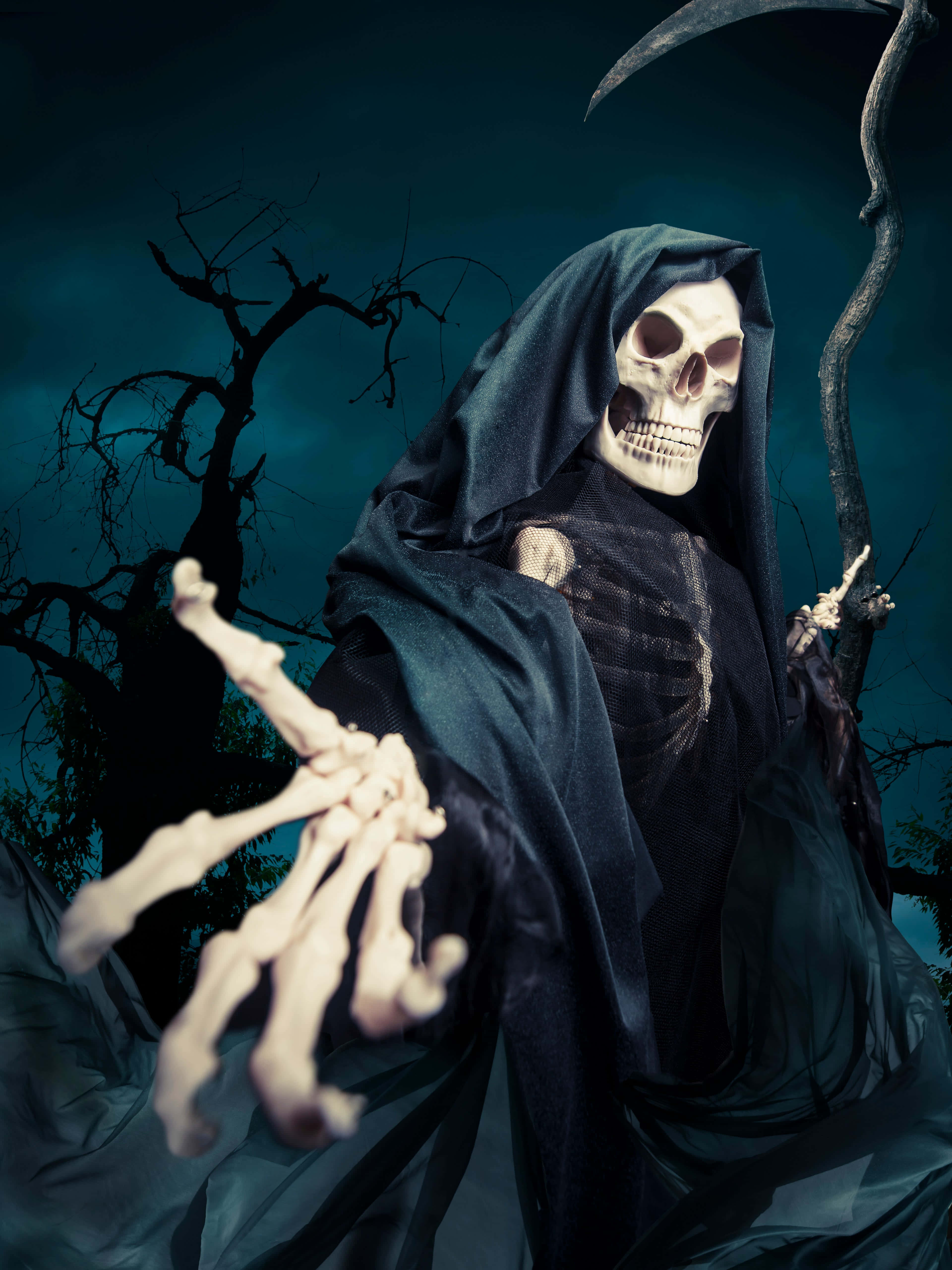 死神 桌布 壁紙 — 一個骷髏死神穿著深色連帽長袍，伸出一隻骨手，背景是陰森的暮色和扭曲的樹木。