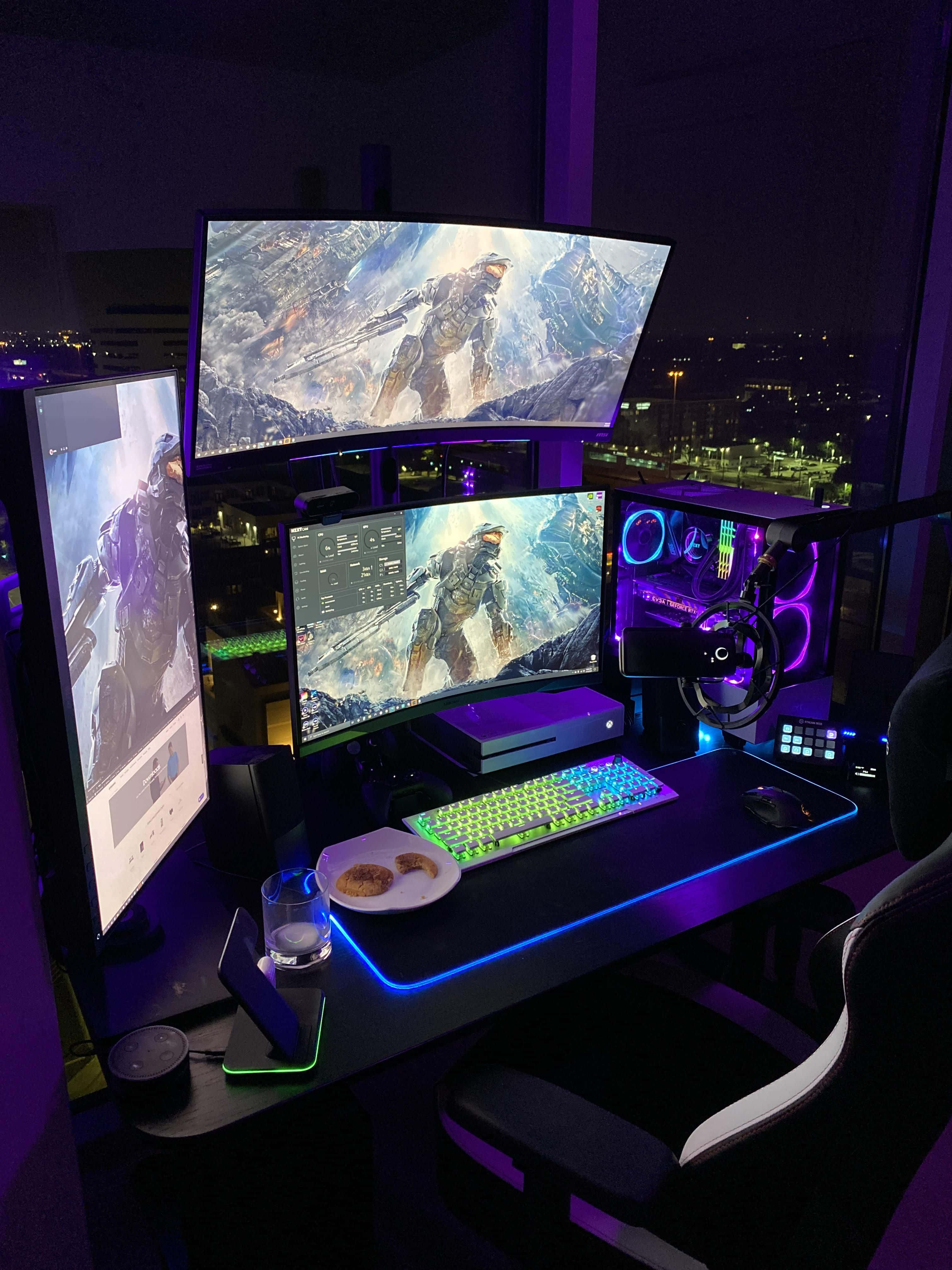 Gaming Pc Setup 桌布 壁紙 — 一個高科技遊戲設置，配備三個顯示器，在夜間紫色環境燈光下展示發光的Halo藝術作品。