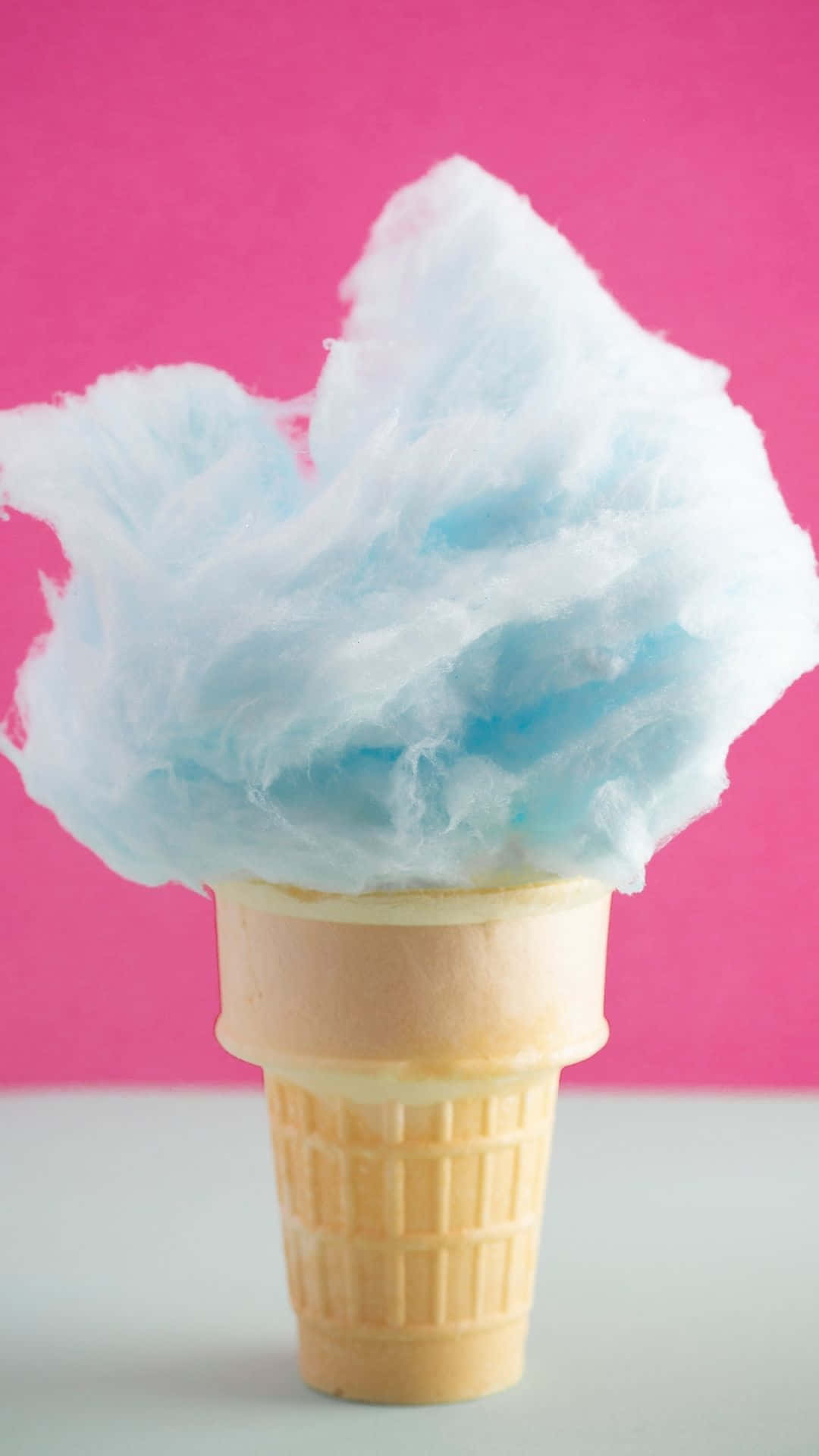Cotton Candy 桌布 壁紙 — 一個鬆軟的藍色棉花糖從窩夫筒中溢出，襯托著充滿活力的粉紅色背景。