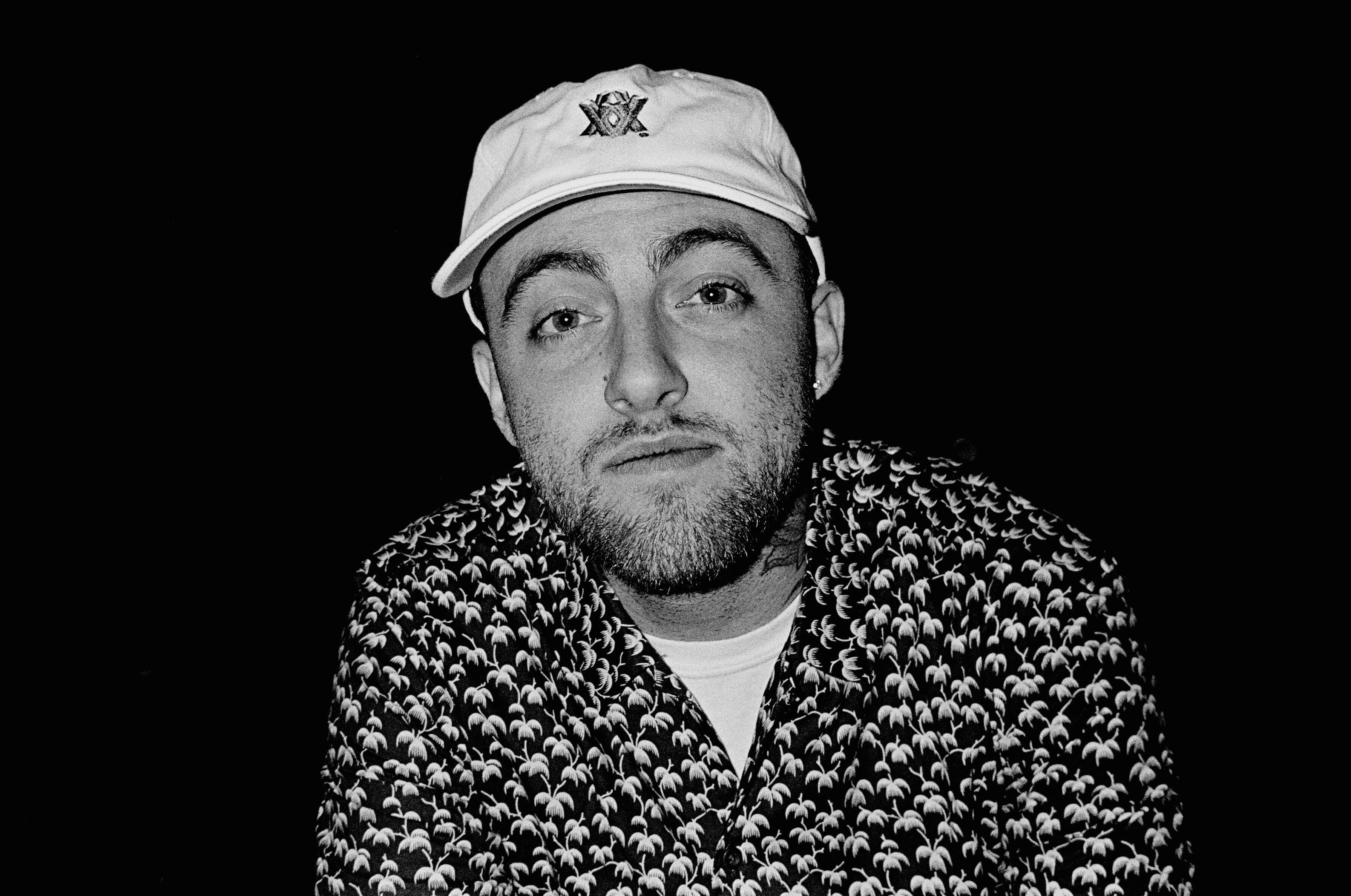 Mac Miller 桌布 壁紙 — 一個鬍鬚男人穿著圖案襯衫和帽子，在深色背景下的黑白肖像。