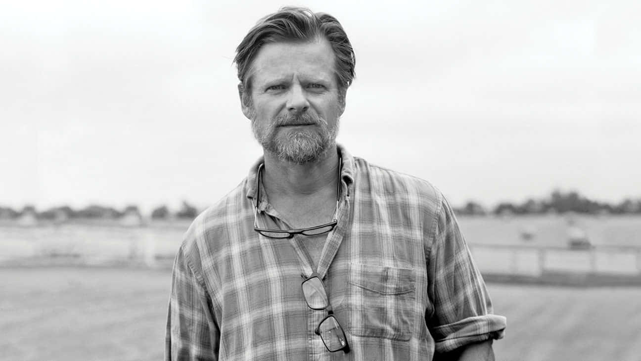 Steve Zahn 桌布 壁紙 — 一個鬍鬚男人穿著格仔襯衫，眼鏡掛在頸上，站在戶外的黑白肖像。