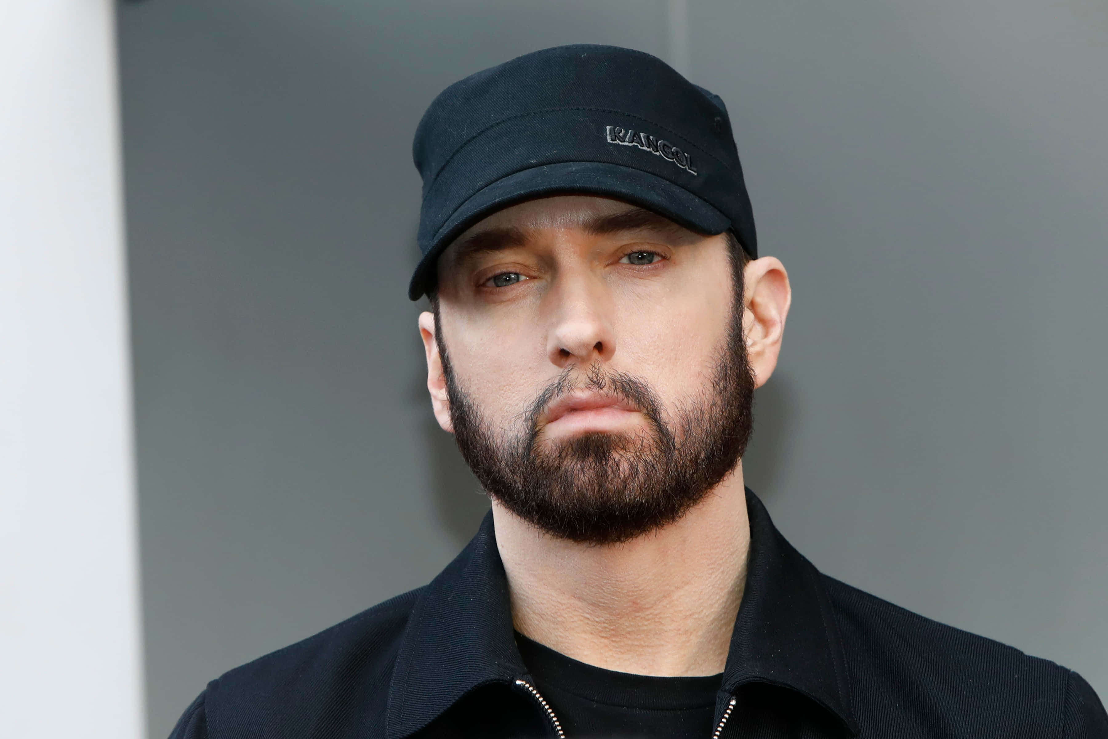 Eminem 桌布 壁紙 — 一個鬍鬚男嘅近距離肖像，戴住黑色帽同外套，背景係灰色。