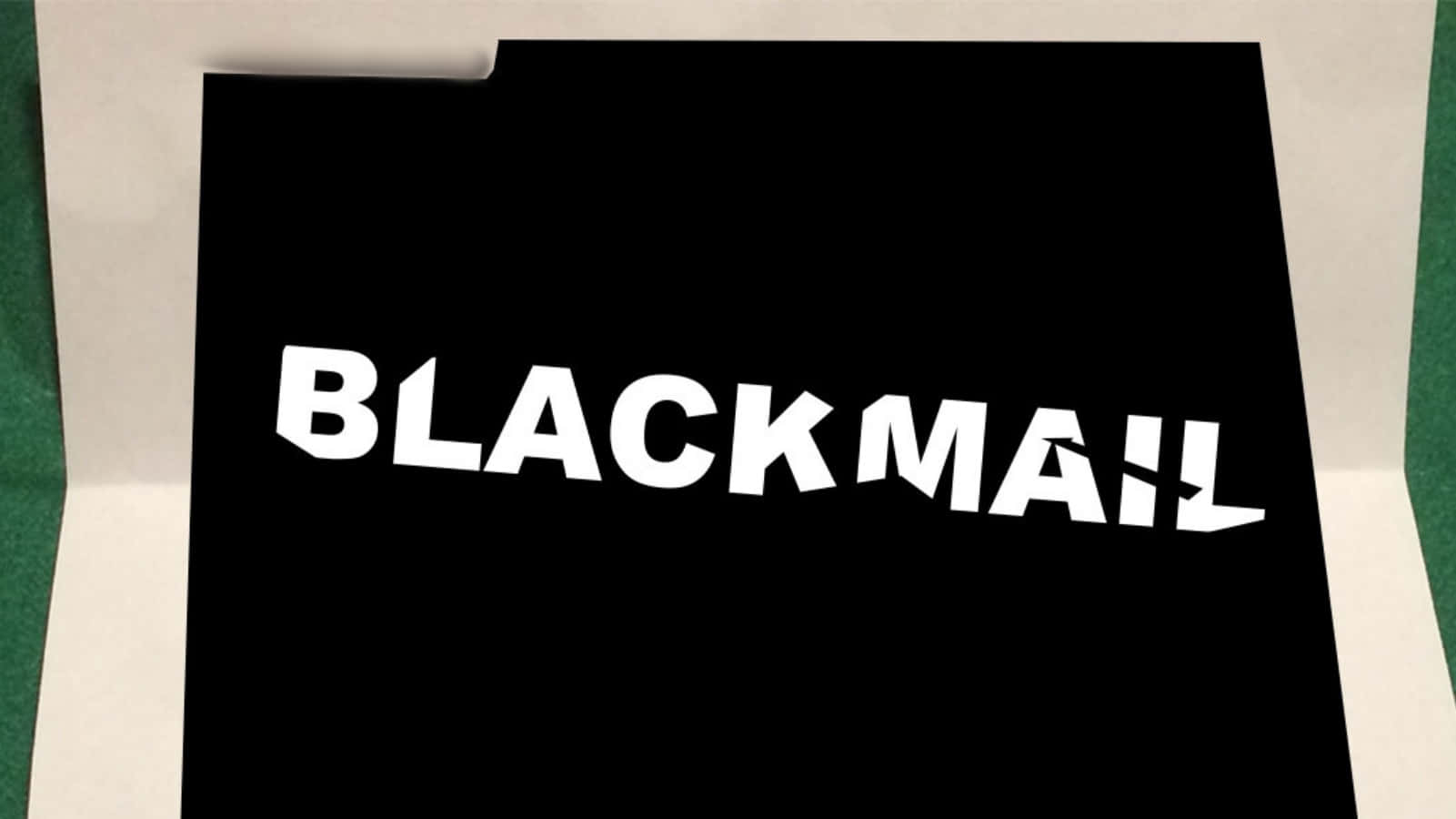Blackmail 桌布 壁紙 — 一個鮮明的黑色文件夾，上面有粗體白色「BLACKMAIL」文字，放在綠色表面上，傳達緊迫和保密。