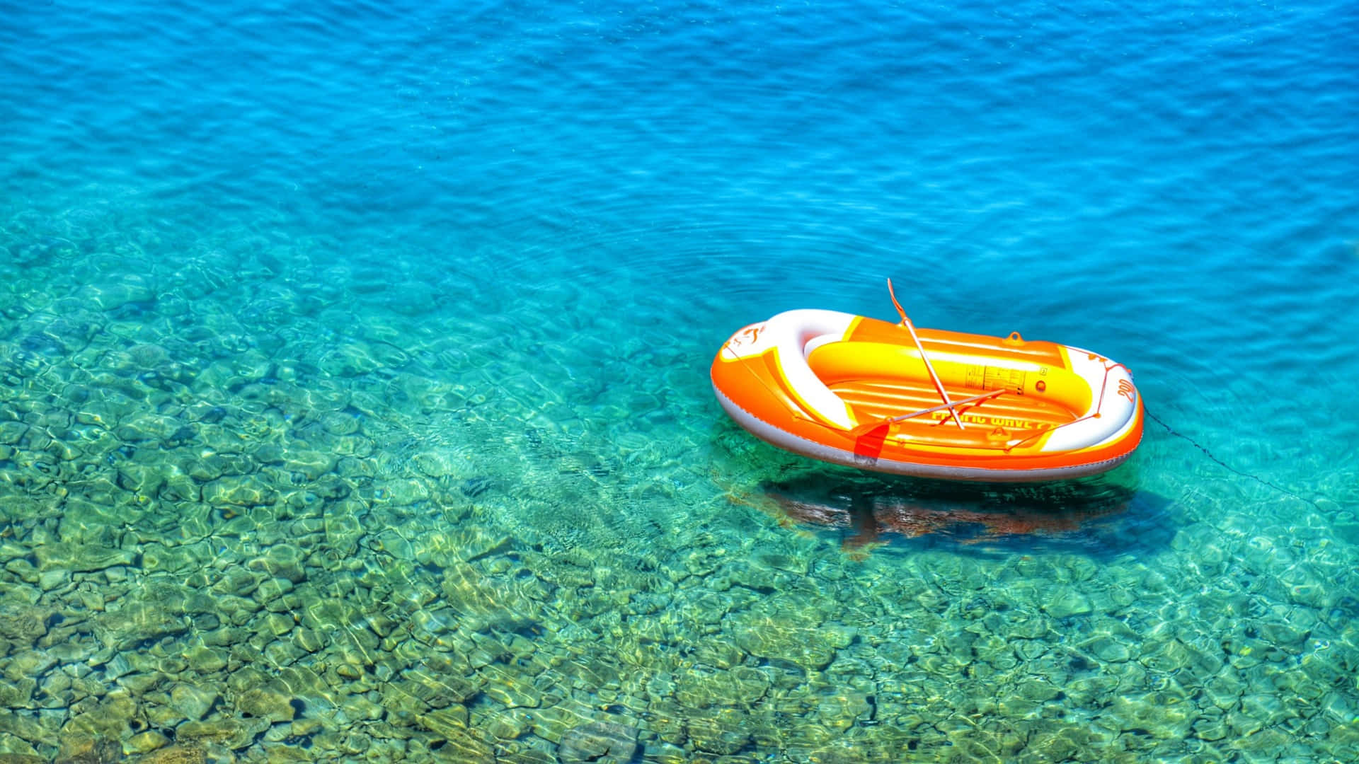 Boating 桌布 壁紙 — 一個鮮橙色充氣筏在清澈見底的碧綠海水上平靜漂浮，露出下方的岩石海床。
