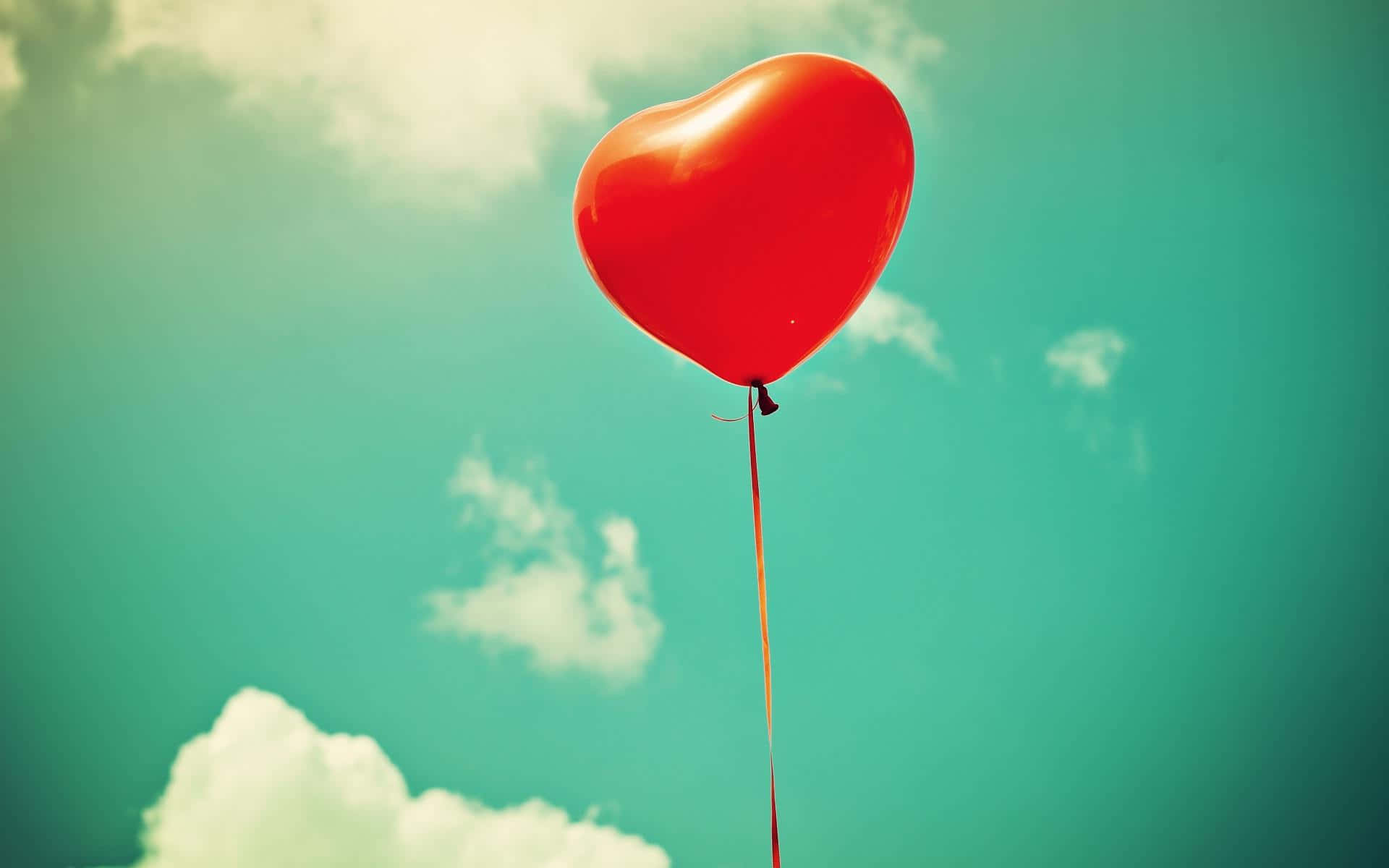 Balloon 桌布 壁紙 — 一個鮮紅色的心形氣球在帶有柔和白色雲朵的藍綠色天空中漂浮。