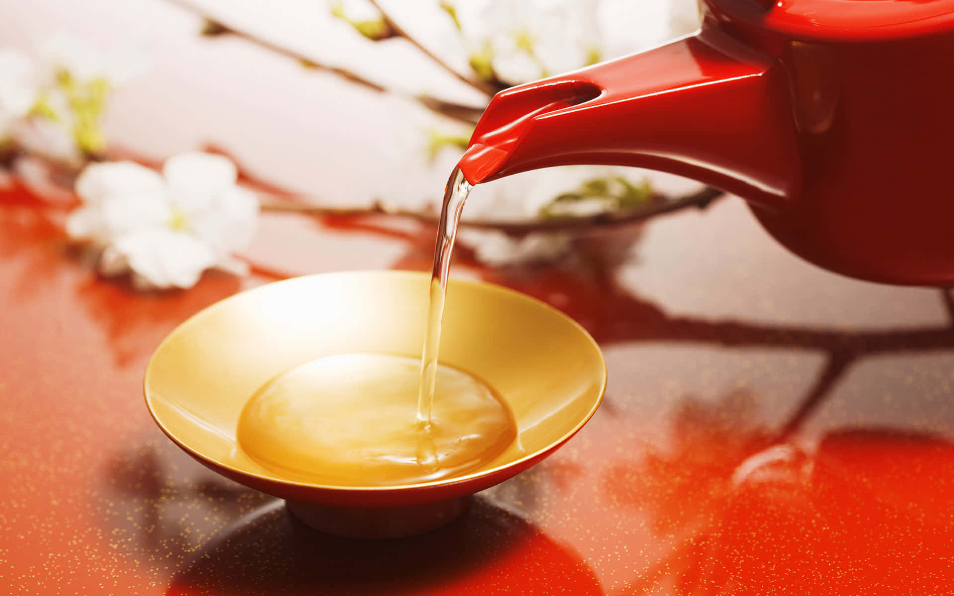 Floral Tea 桌布 壁紙 — 一個鮮紅色的茶壺將冒煙的液體倒入一個金色的杯子中，背景是柔和的白色櫻花。